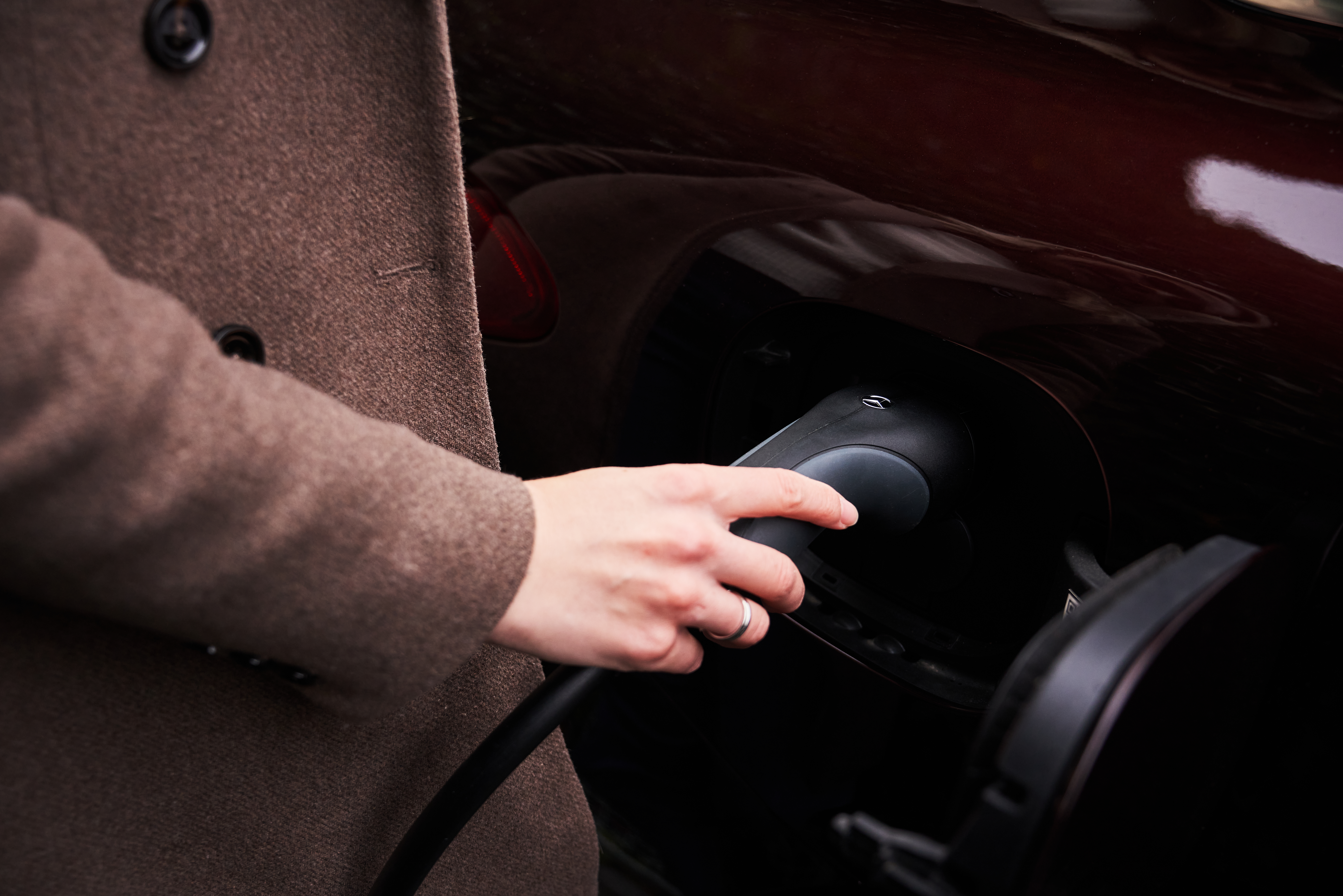 Väggmonterad laddbox | laddningsutrustning | Mercedes-Benz Kvinna sätter i laddkabeln i sin elektriska Mercedes-Benz.