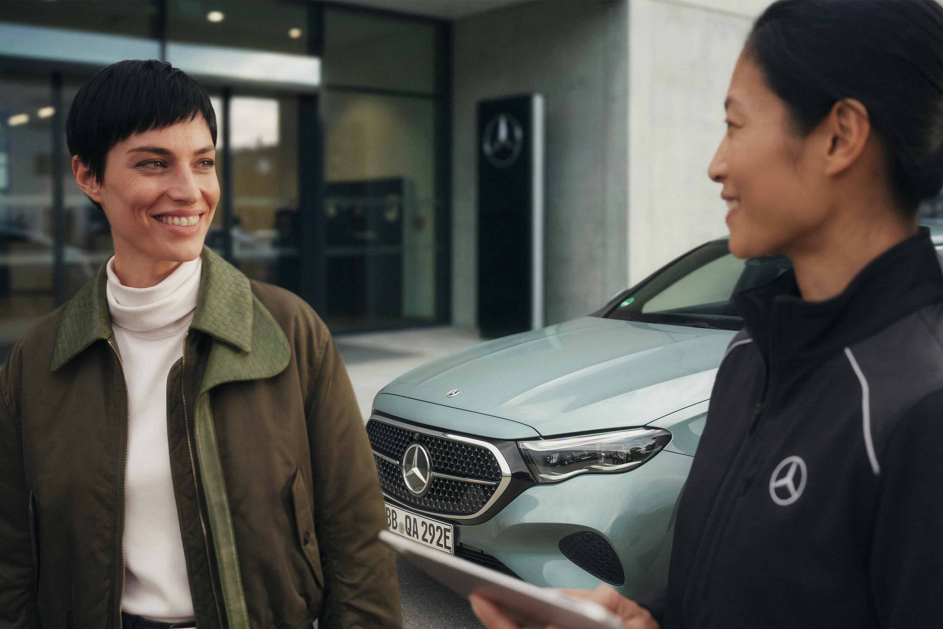 Certifierade begagnade bilar | Mercedes-Benz Mercedes-Benz-återförsäljare pratar med en kund utanför ett showroom.
