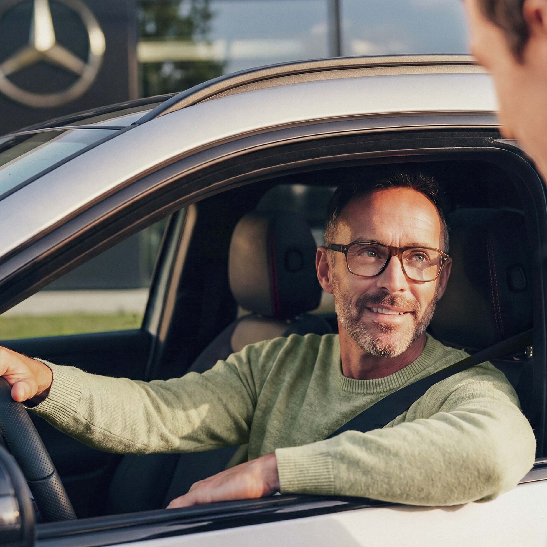 Man sitter i sin begagnade Mercedes-Benz och pratar genom fönstret med återförsäljaren.