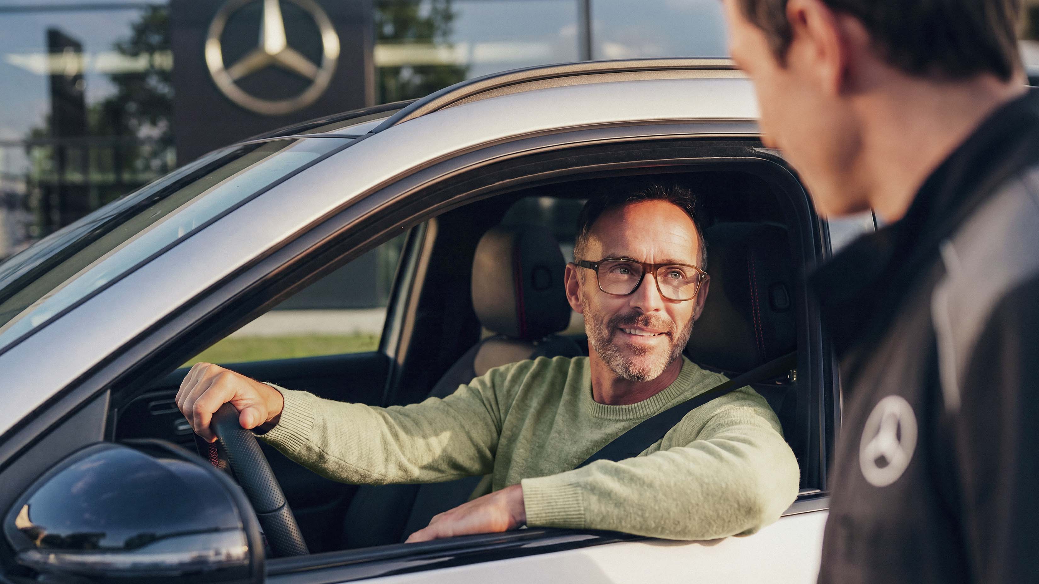 Certifierade begagnade bilar | Mercedes-Benz Man sitter i sin begagnade Mercedes-Benz och pratar genom fönstret med återförsäljaren.