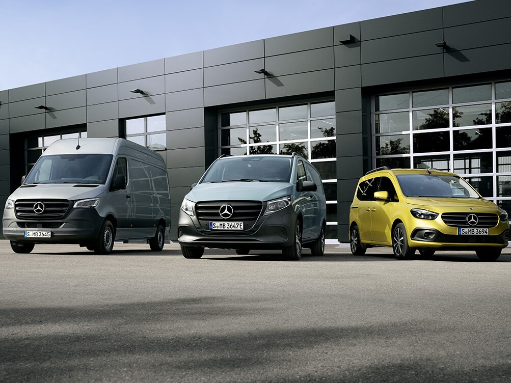 Tre Mercedes-Benz transportbilar sida vid sida framför ett verkstad