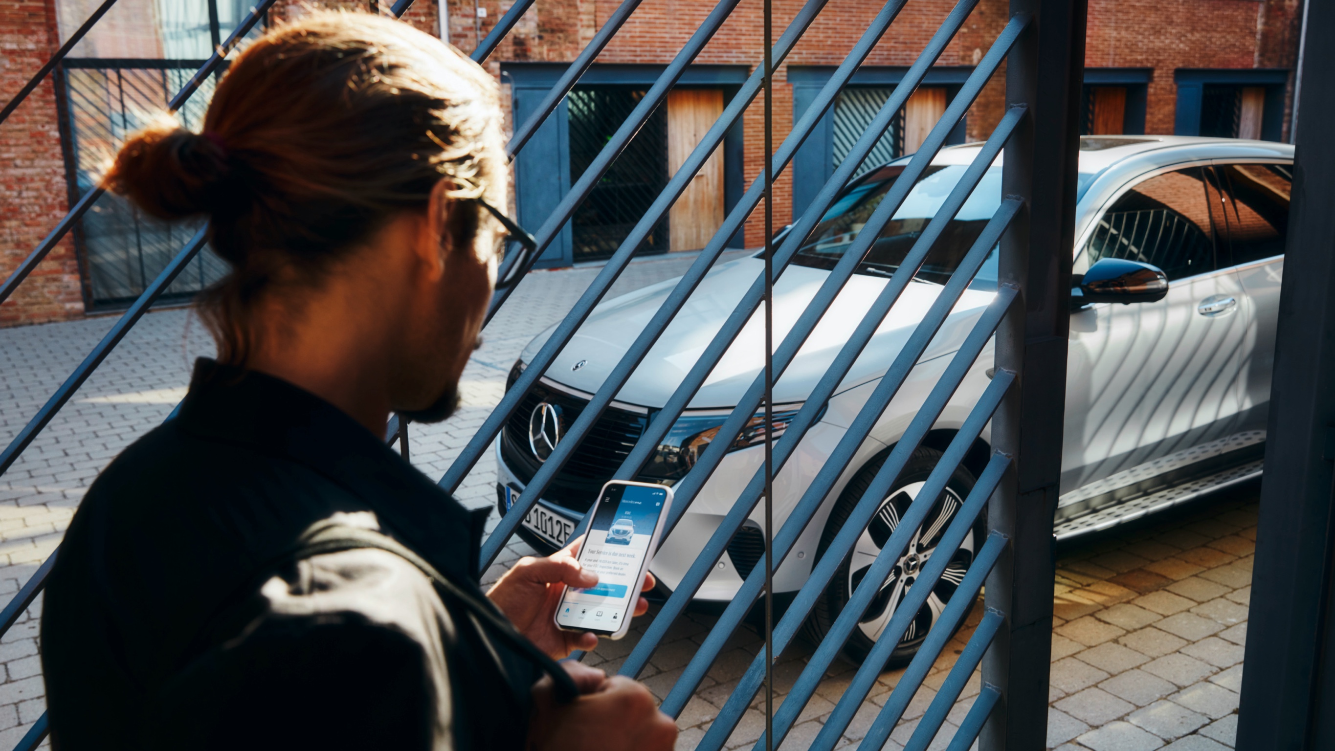 Mercedes-Benz app | Mercedes-Benz Man står framför sin Mercedes-Benz SUV och använder Mercedes-Benz app