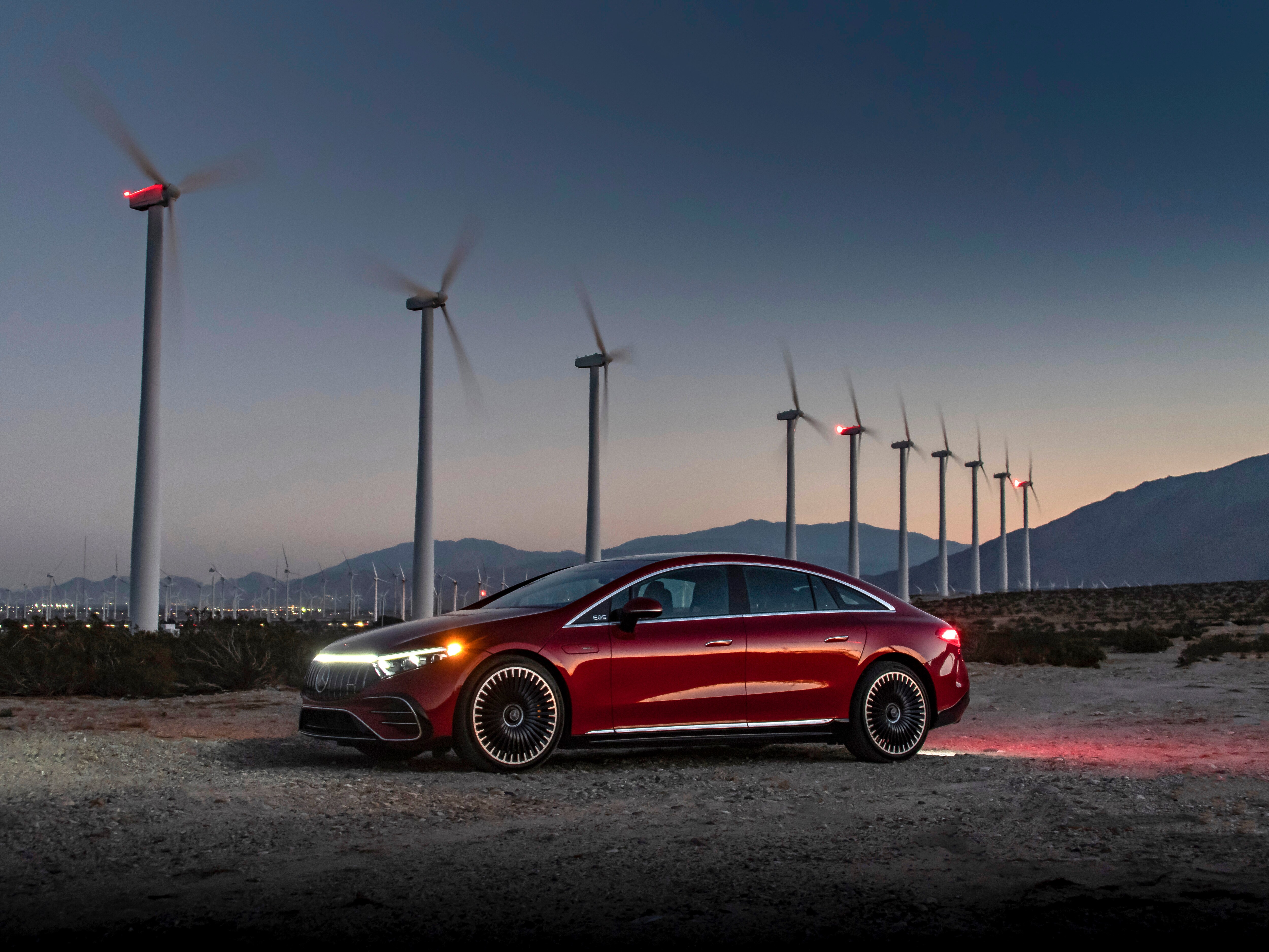 Röd Mercedes-Benz EQS Sedan parkerad framför vindkraftverk