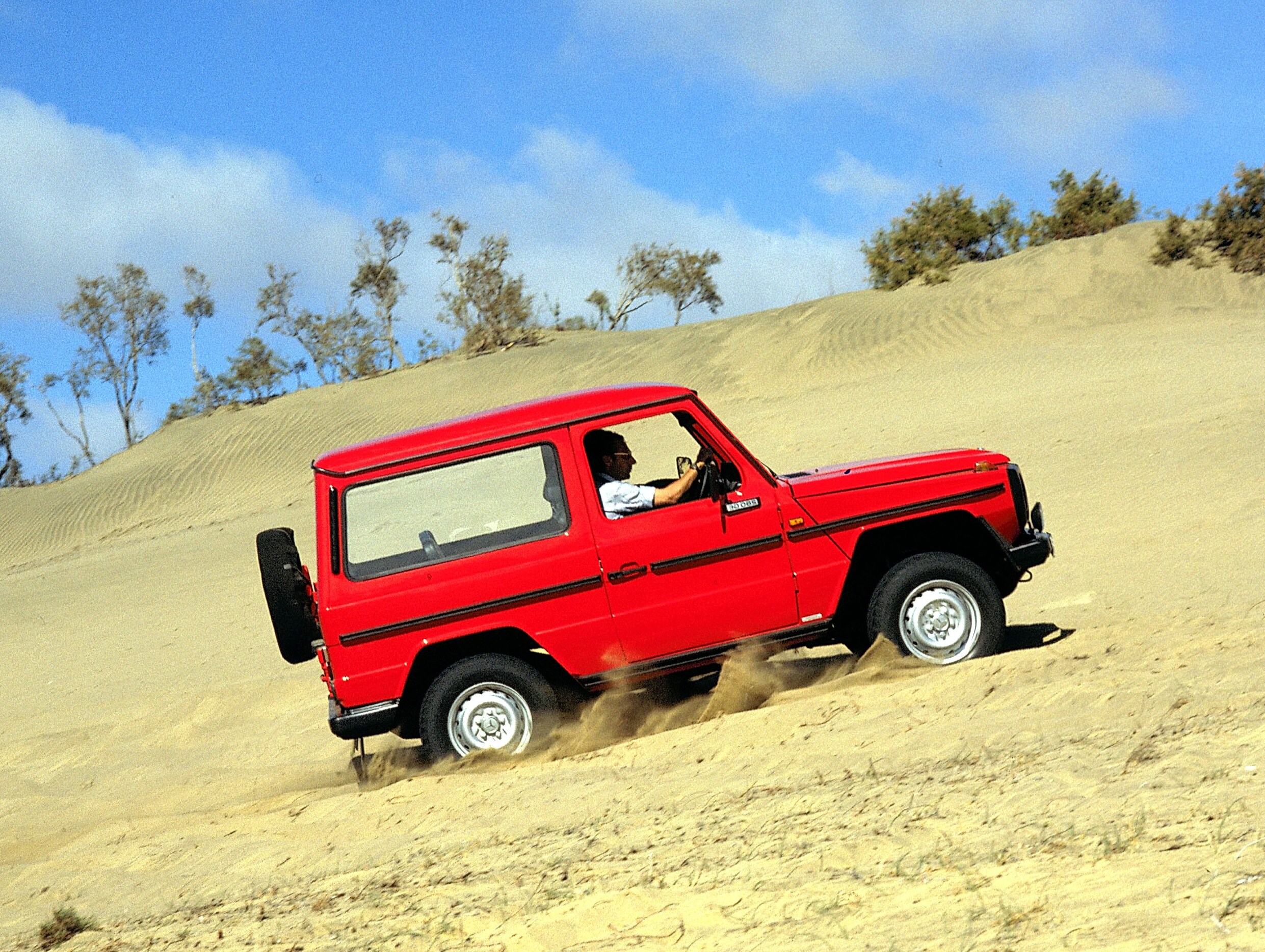 Röd Mercedes-Benz G-Klass i modellserie 460 kör uppför en sandbacke