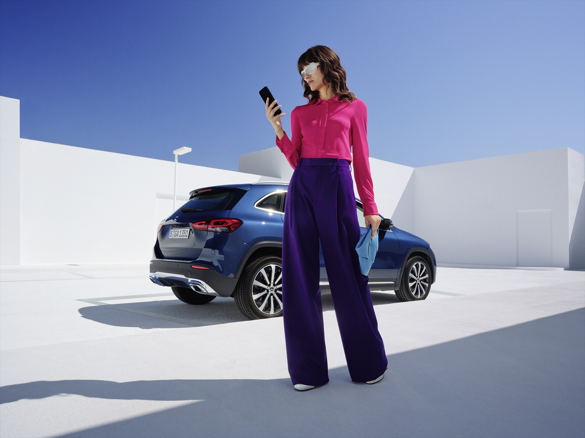 En kvinna står framför Mercedes-Benz GLA och tittar på sin telefon.