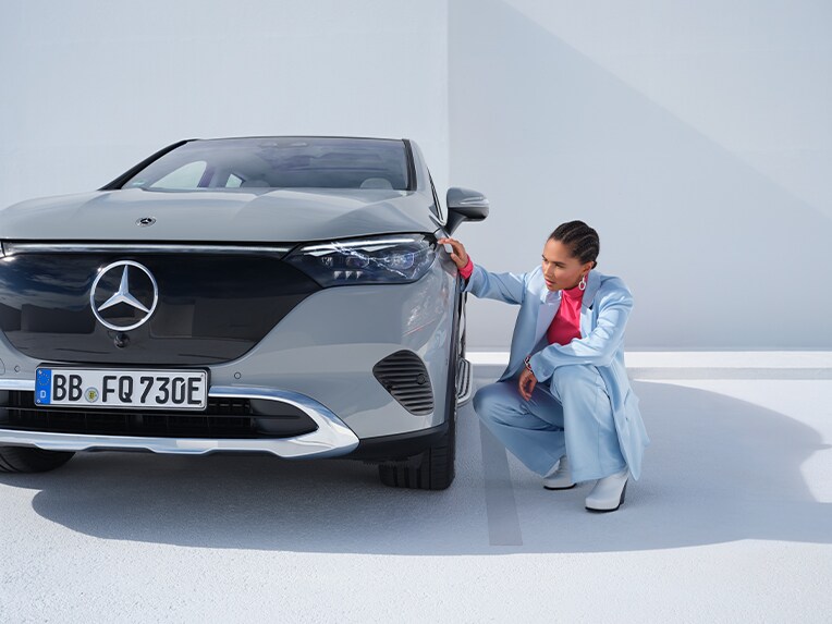 Kvinna inspekterar fronten på sin gråa Mercedes-Benz elbil.