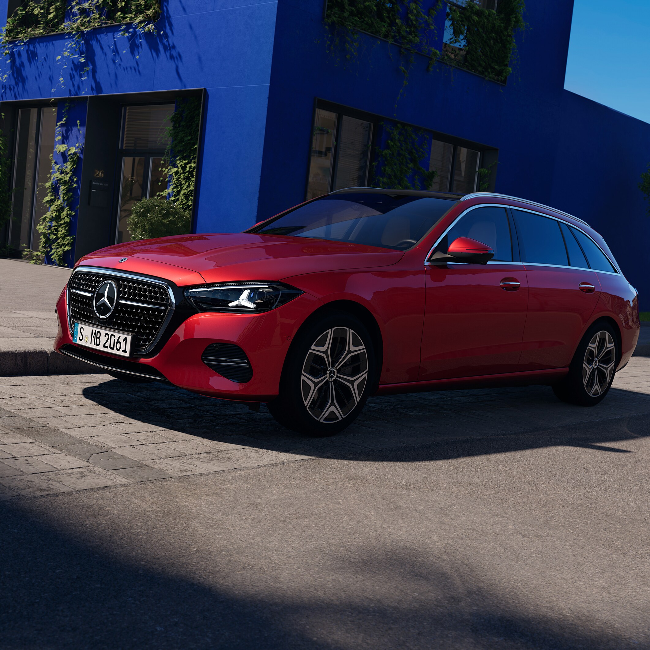 En röd Mercedes-Benz C-Klass Kombi kör förbi en blå byggnad.