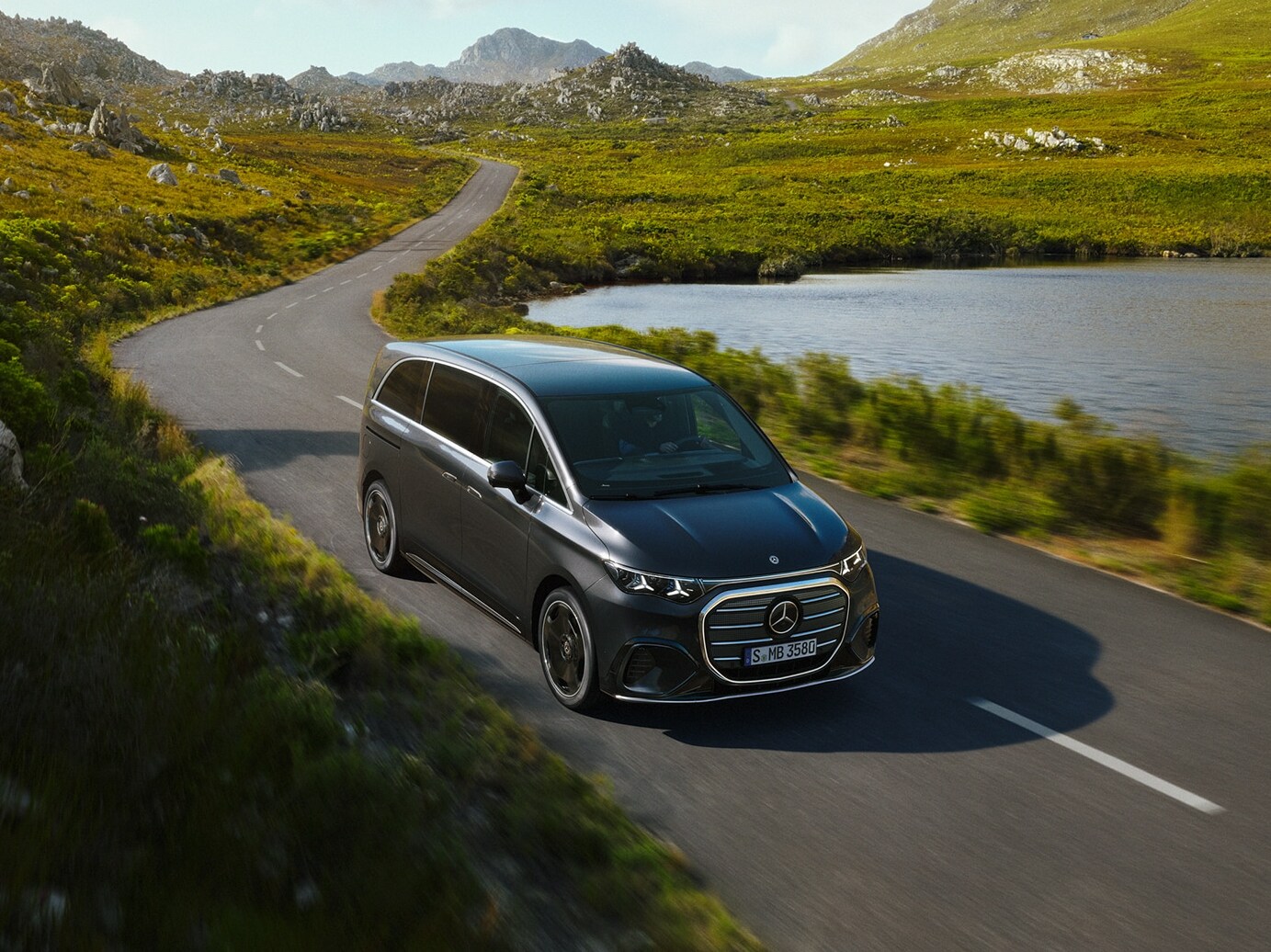 Mercedes-Benz VLE kör längs en naturskön väg vid en sjö och visar förstklassig komfort, rymlighet och förfinad mångsidighet för resor.