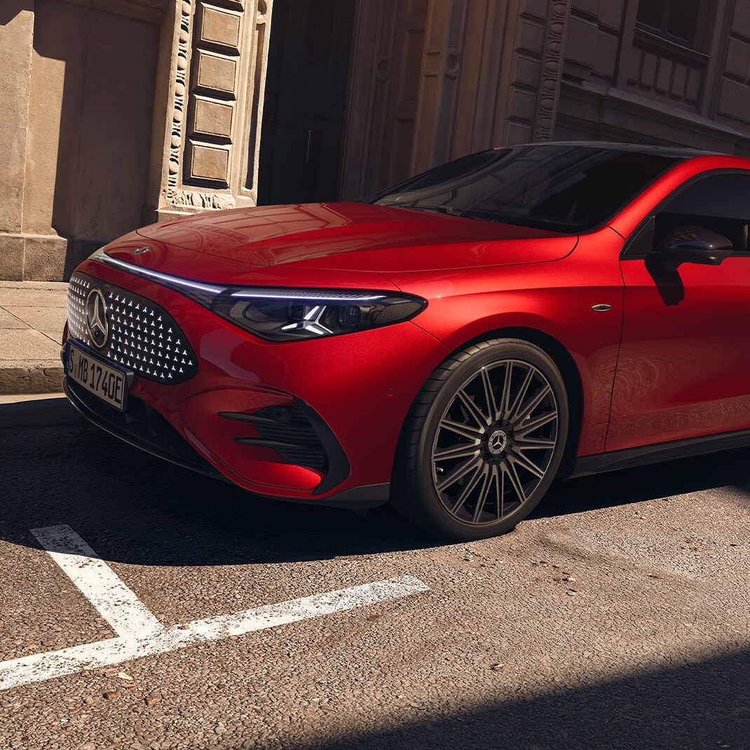Röd helelektrisk Mercedes-Benz CLA parkerad vid trottoarkanten framför en byggnad