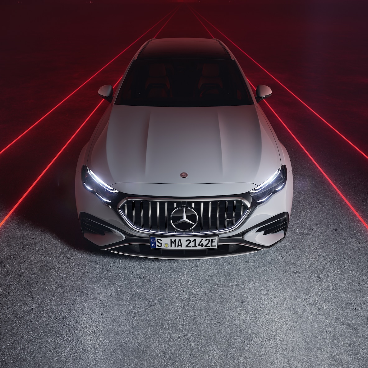 Mercedes-AMG E 53 HYBRID 4MATIC+ framifrån mot en röd bakgrund, sedd uppifrån.