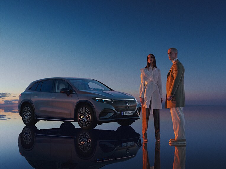 Två personer står vid en Mercedes-Benz SUV med solnedgång i bakgrunden.