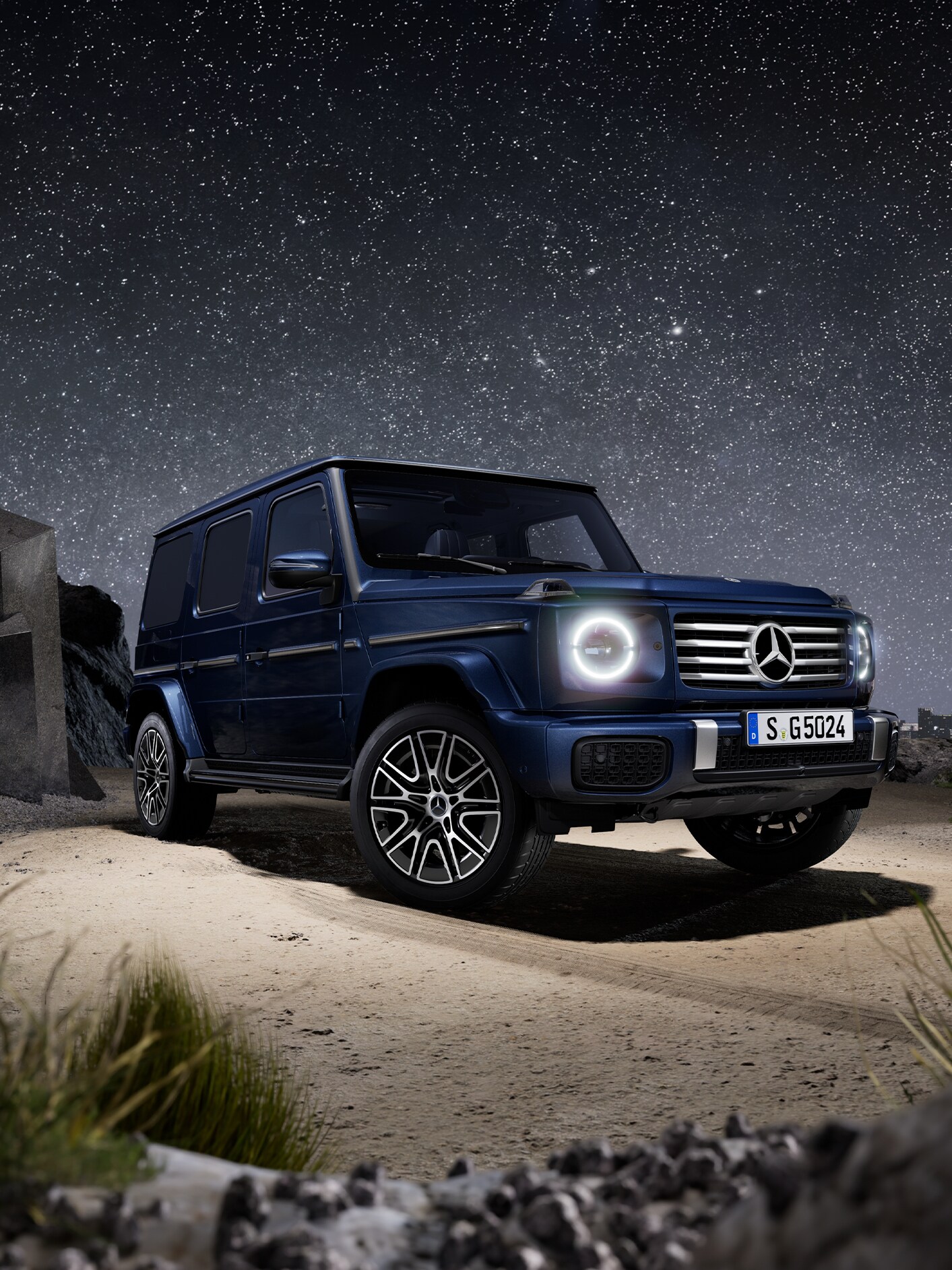 Mörkblå Mercedes-Benz G-Klass sedd snett framifrån under stjärnklar natthimmel