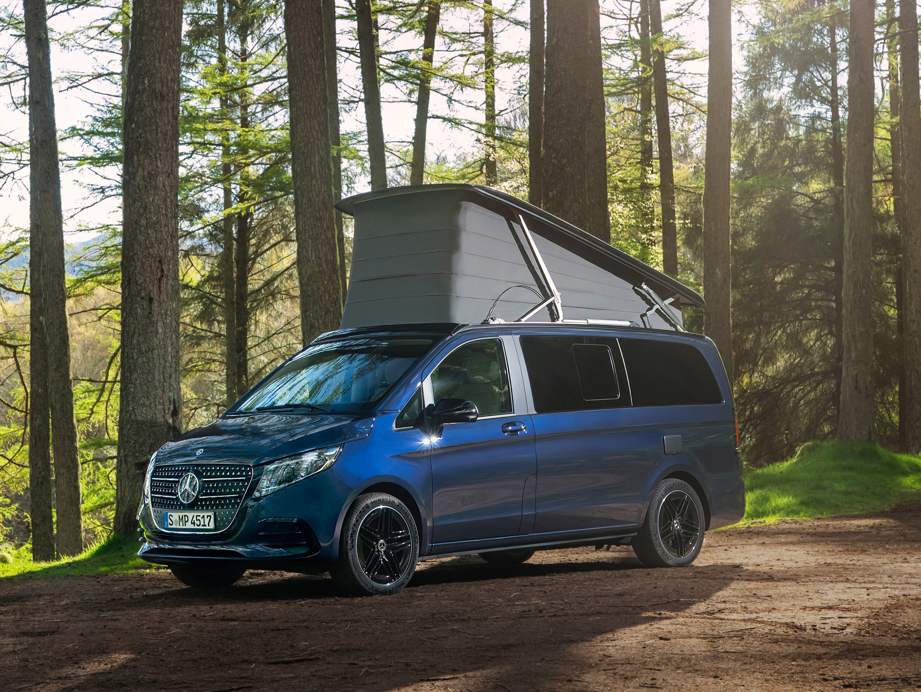 Blå Mercedes-Benz Marco Polo med uppfällt pop-up tak i skog.
