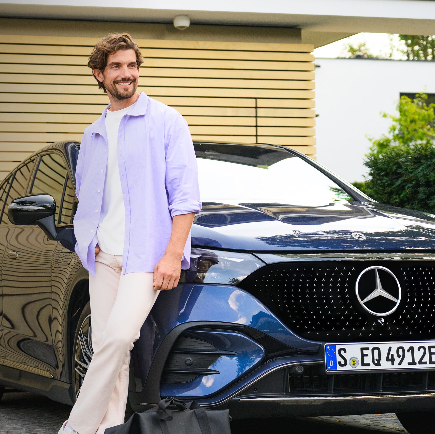 Man som lutar sig mot ett Mercedes-Benz fordon framför sitt hus.
