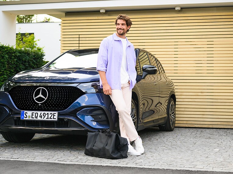 En man som lutar sig mot ett Mercedes-Benz fordon och tittar på himlen.