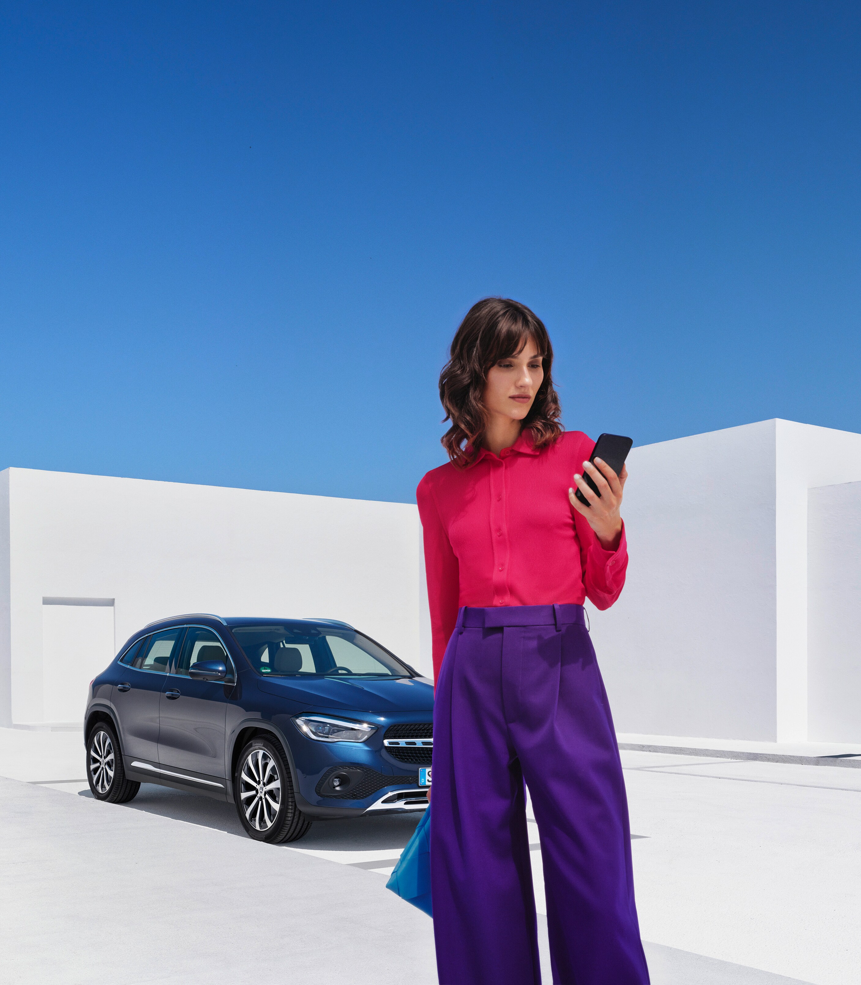 En kvinna står framför sin Mercedes-Benz EQA och kollar i sin smartphone.