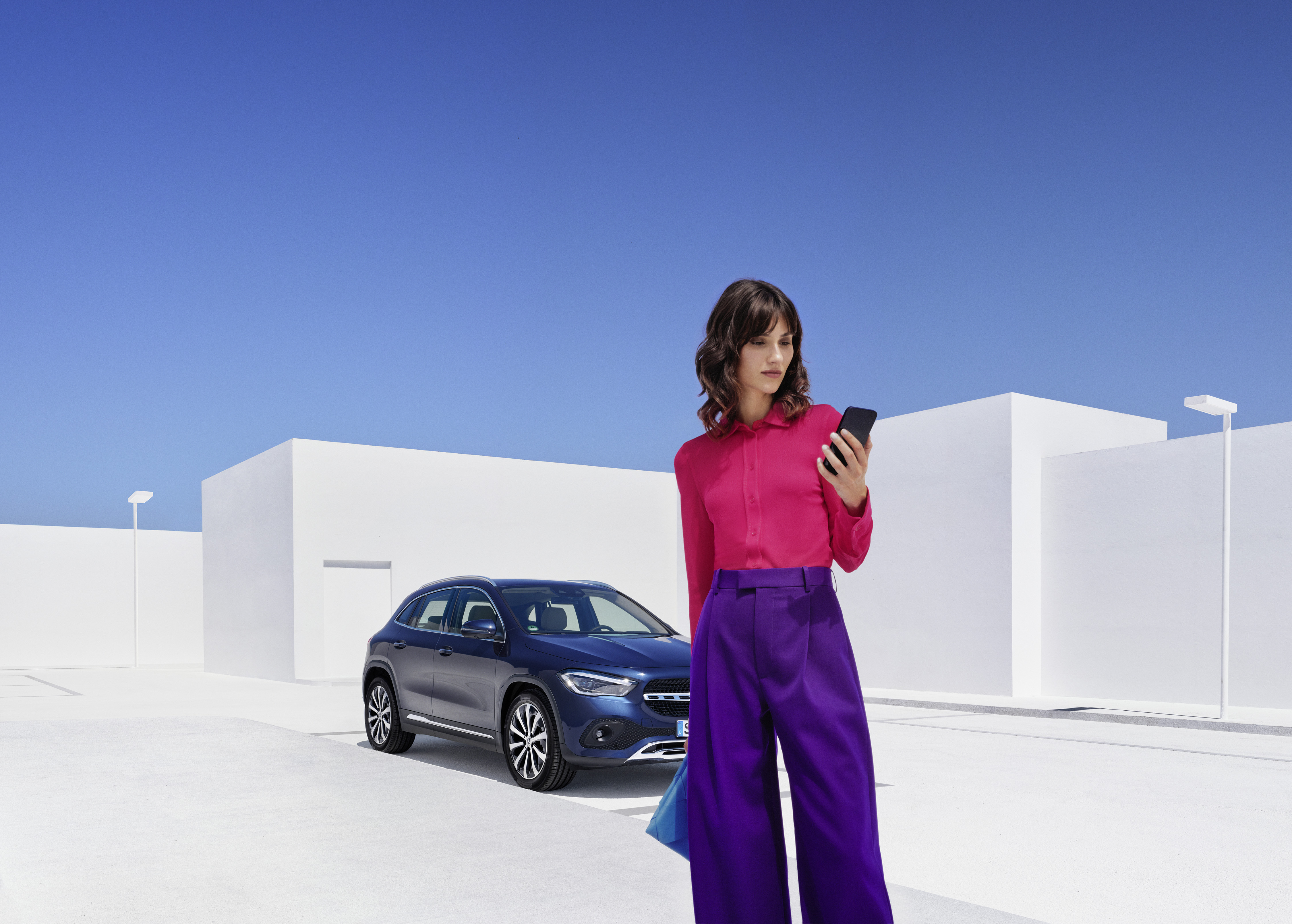 Vägassistans | Mercedes-Benz En kvinna står framför sin Mercedes-Benz EQA och kollar i sin smartphone.