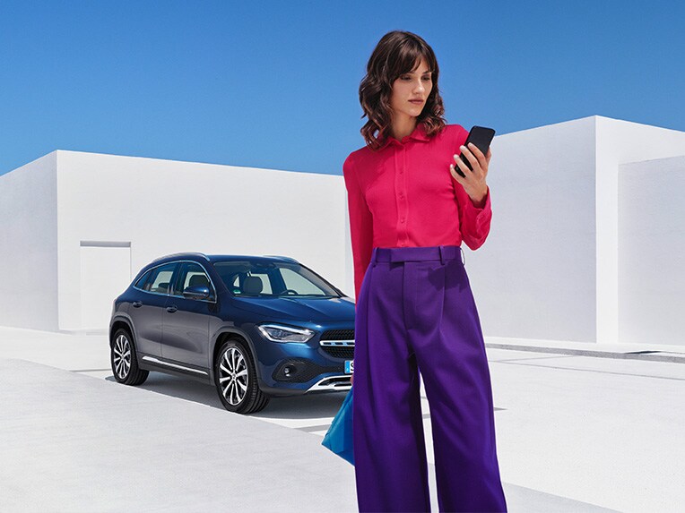 Kvinna med mobiltelefon framför blå parkerad Mercedes-Benz bil