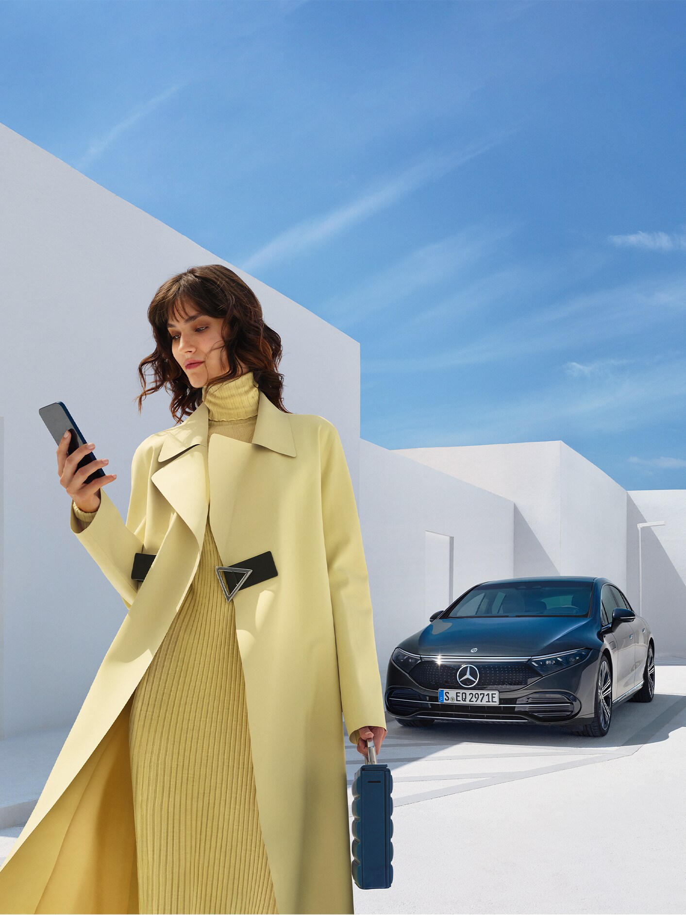 Kvinna står vid sin parkerade Mercedes-Benz EQE och tittar på sin telefon.