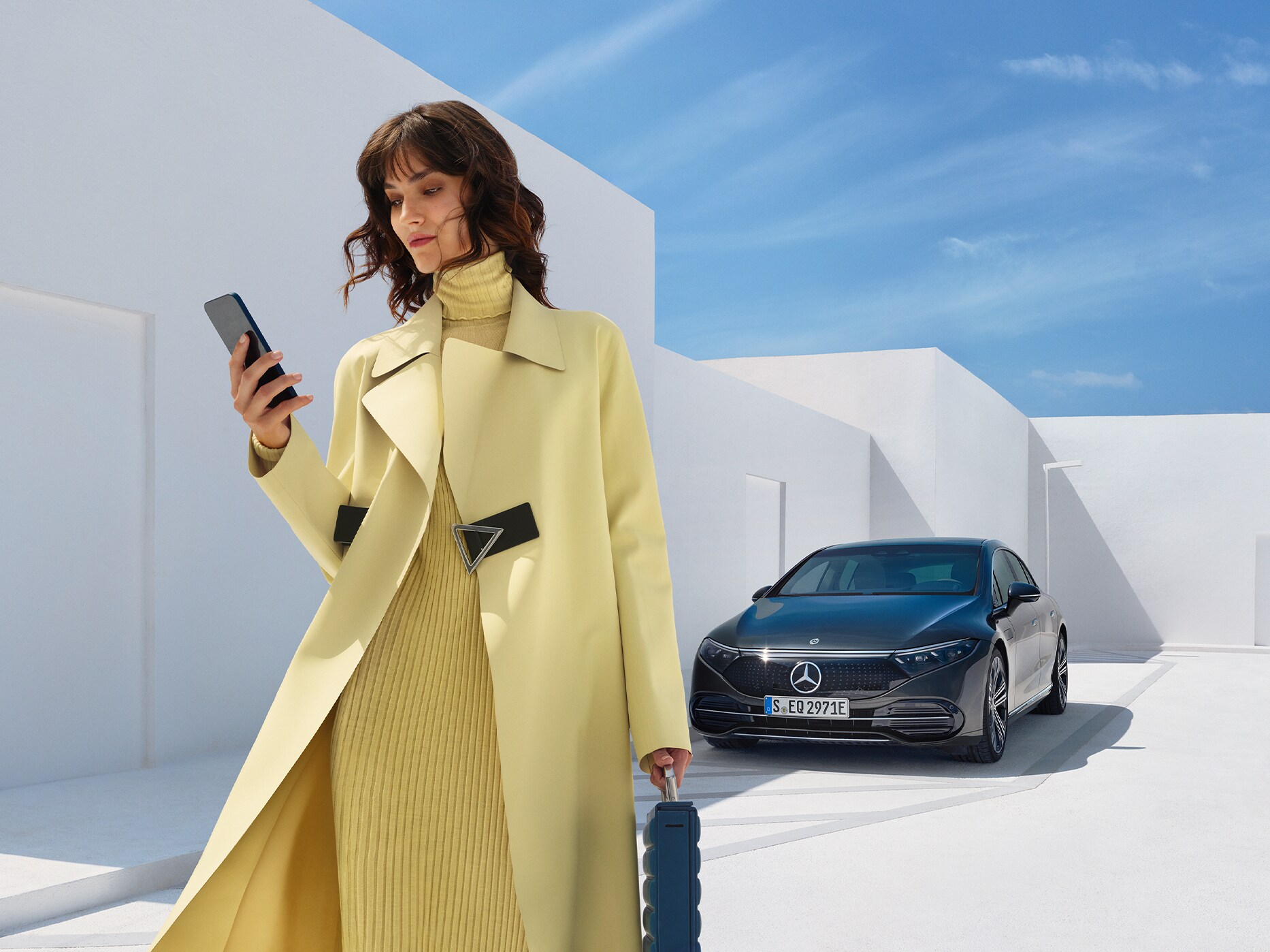 Kvinna står vid sin parkerade Mercedes-Benz EQE och tittar på sin telefon.