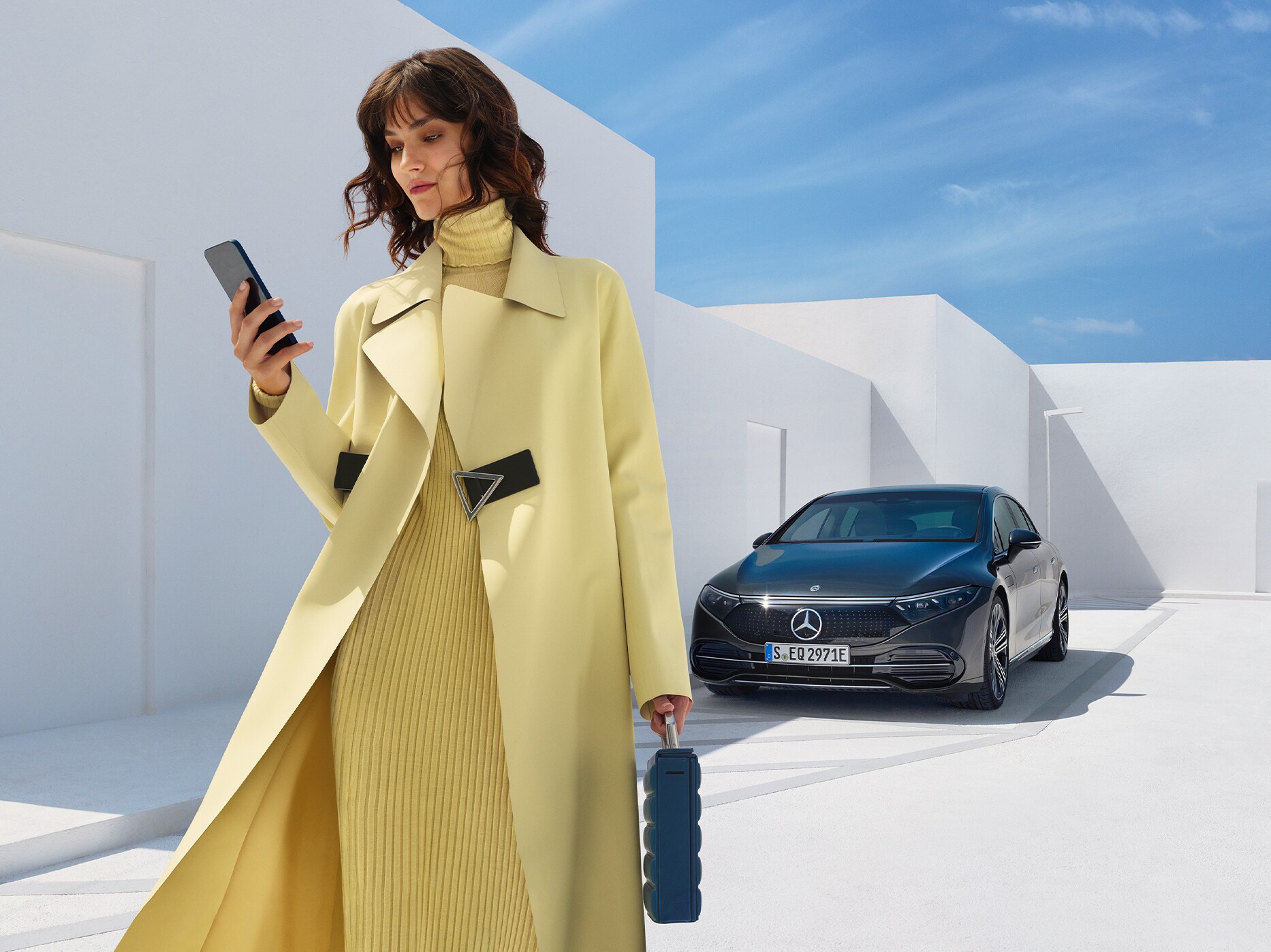 Kvinna står vid sin parkerade Mercedes-Benz EQE och tittar på sin telefon.