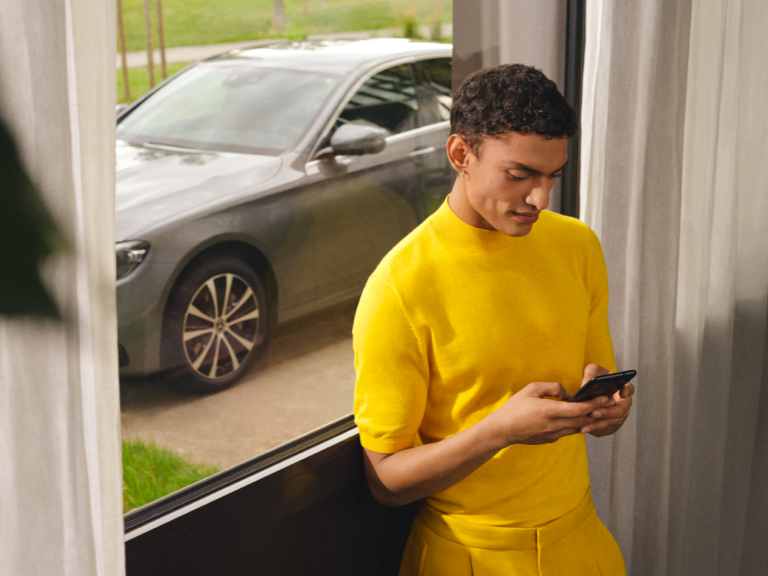 Mercedes-Benz kundtjänst | Mercedes-Benz Finans Person använder sin smartphone inomhus framför sin Mercedes-Benz