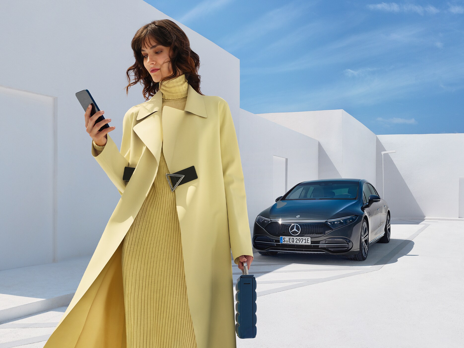 Kvinna står vid sin parkerade Mercedes-Benz EQE och tittar på sin telefon.