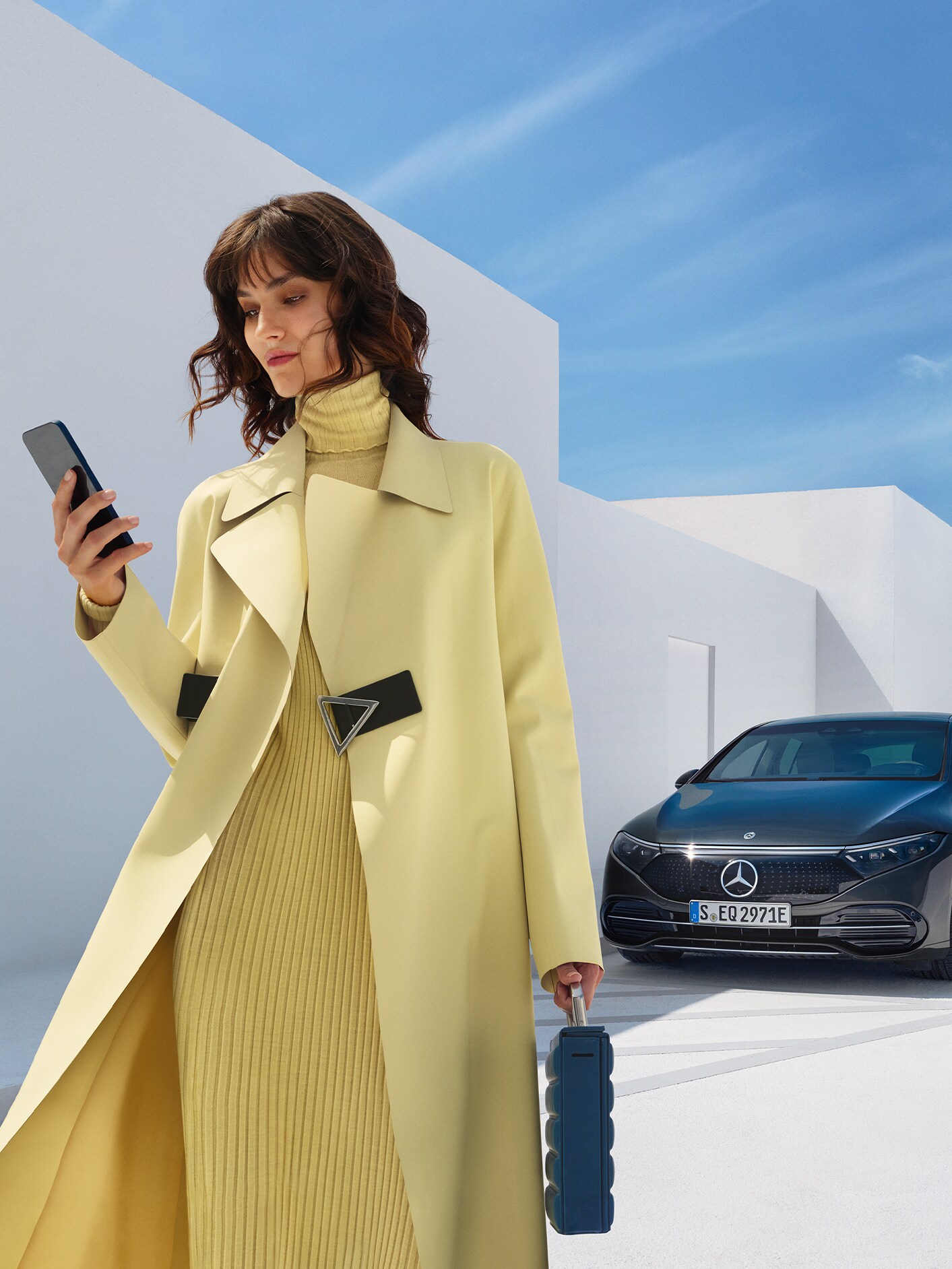 En kvinna i gula kläder står framför en EQS Sedan från Mercedes-Benz.