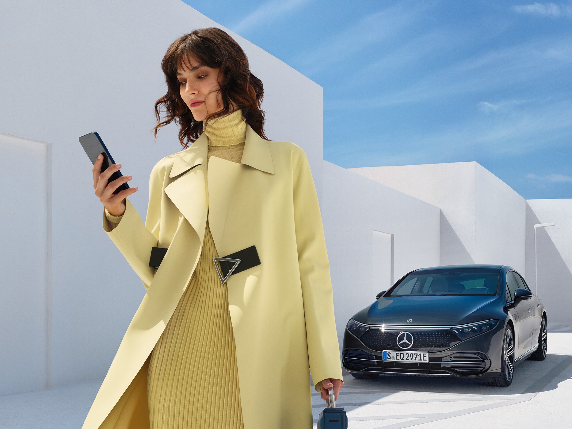 En kvinna i gula kläder står framför en EQS Sedan från Mercedes-Benz.