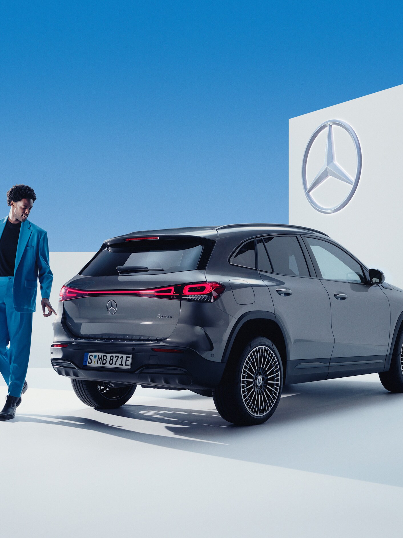 En person i kostym står framför en grå Mercedes-Benz EQA.