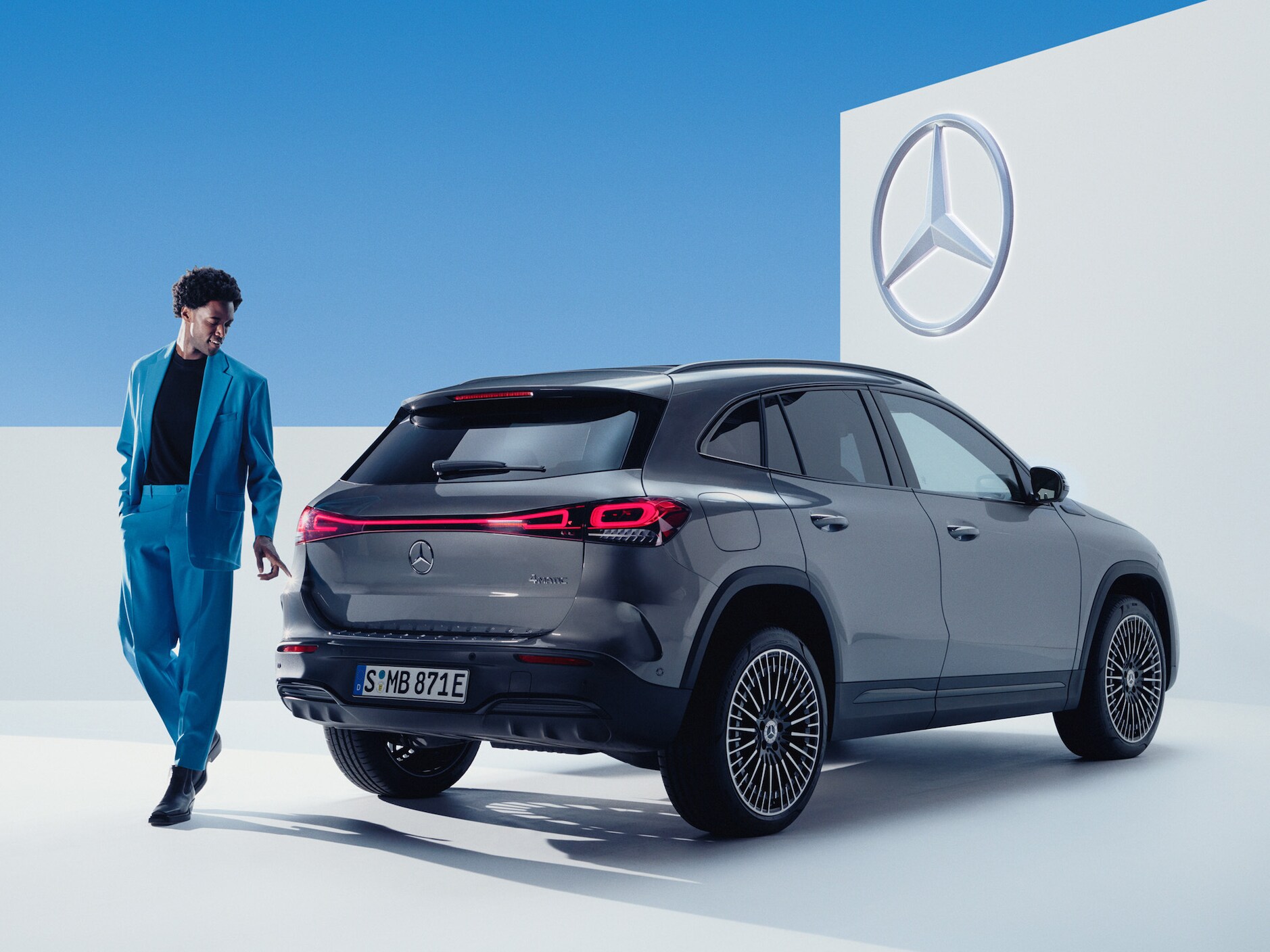 En person i kostym står framför en grå Mercedes-Benz EQA.