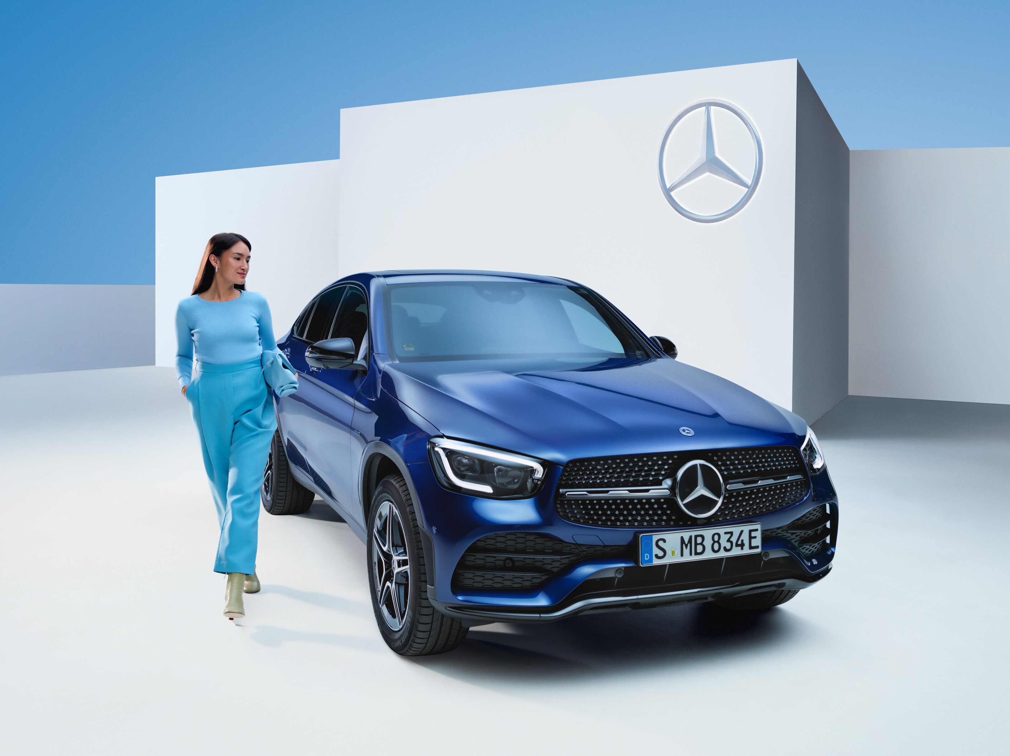 Kvinna klädd i blått står sidan om en blå Mercedes-Benz GLC SUV.