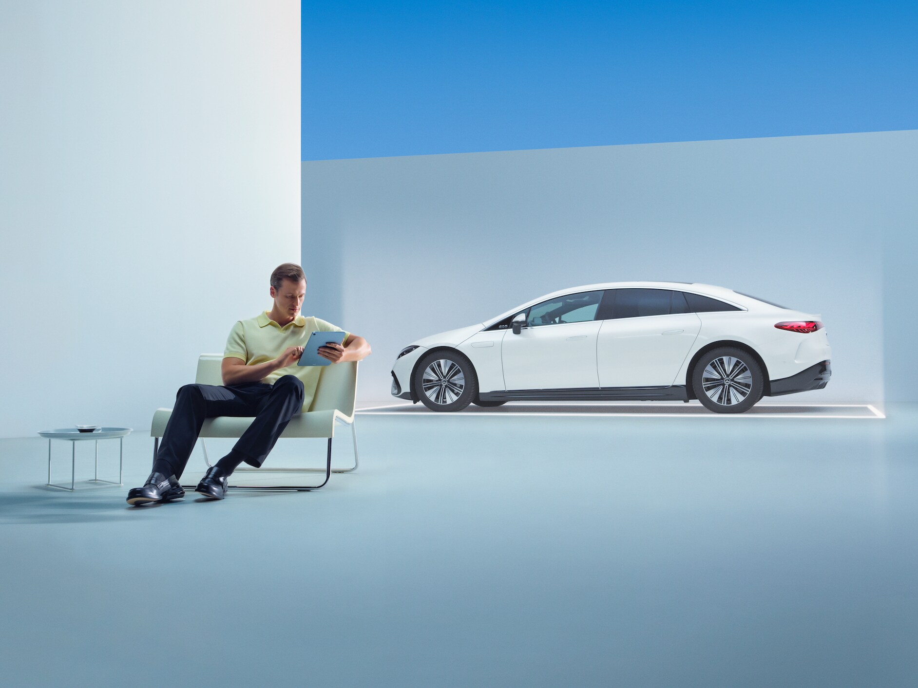 Person med surfplatta utforskar Mercedes-Benz utbud av bilar framför en vit EQS