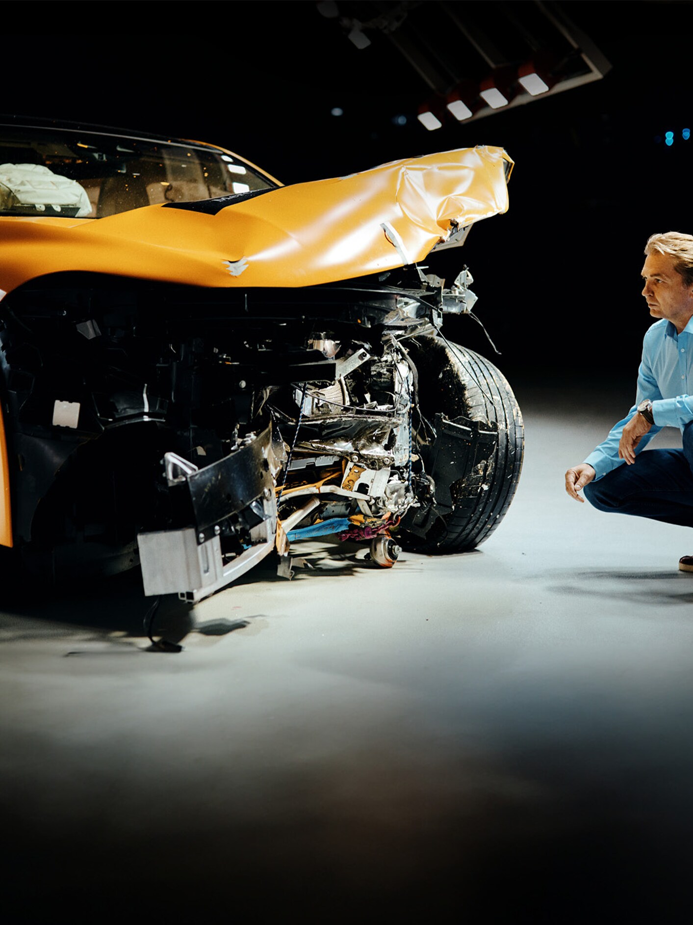 En krocktestsexpert undersöker en frontalkrockad Mercedes-Benz-bil medan han sitter på huk bredvid den.