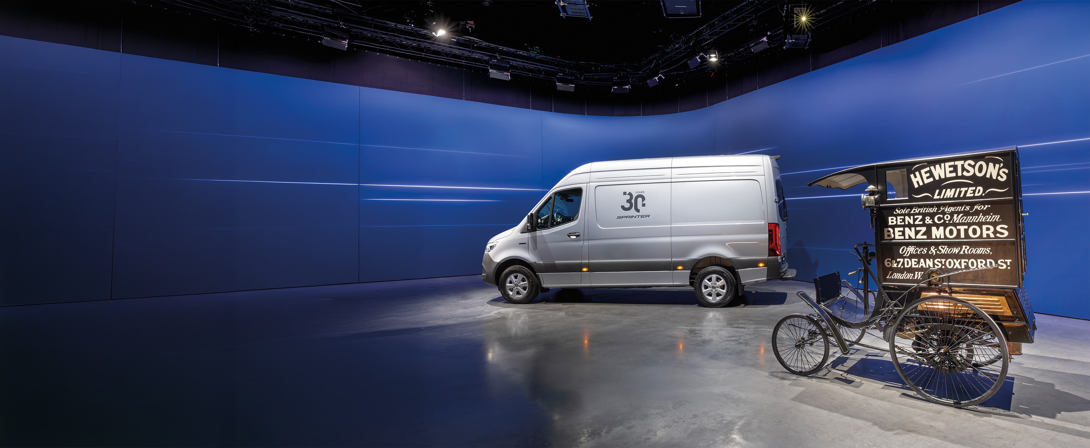Historia | Transportbilar | Mercedes-Benz Transportbilen Mercedes-Benz Sprinter och den historiska transportbilen Benz visas i en modern bilhall
