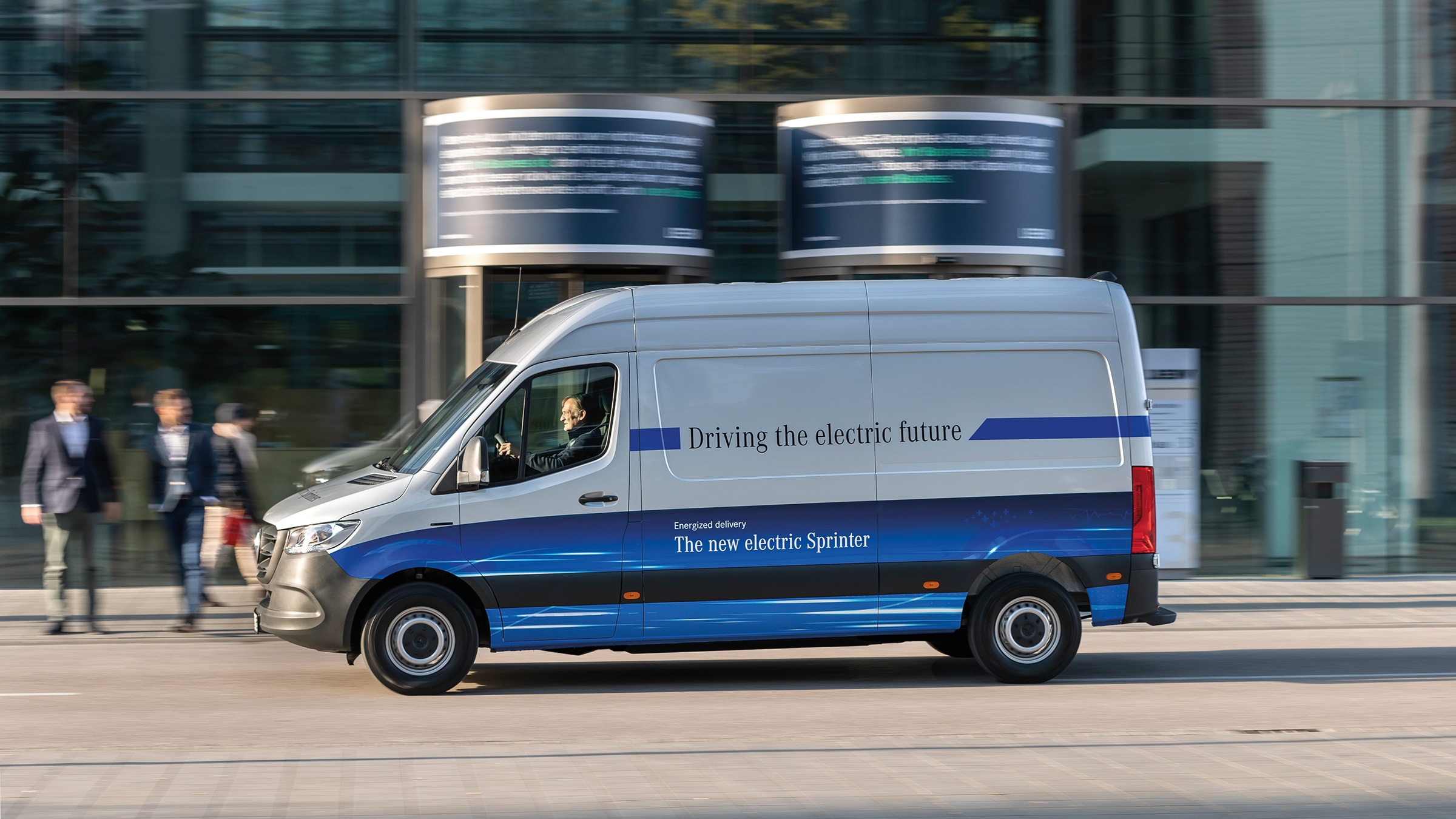 Skåpbilen eSprinter i andra generationen | Transportbilshistoria | Mercedes-Benz Skåpbilen Mercedes‑Benz eSprinter kör på en modern stadsgata