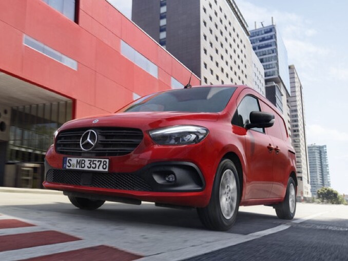 Röd Mercedes-Benz Citan skåpbil kör genom en storstad.