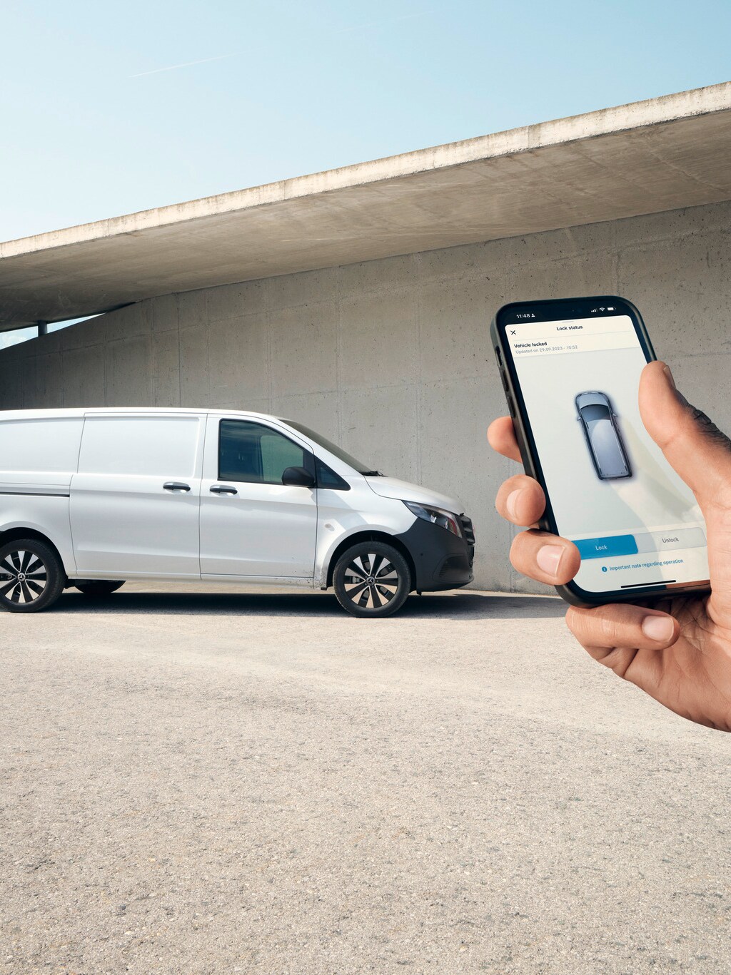 Hand håller en smartphone med Mercedes-Benz appen, Vito Skåpbil i bakgrunden