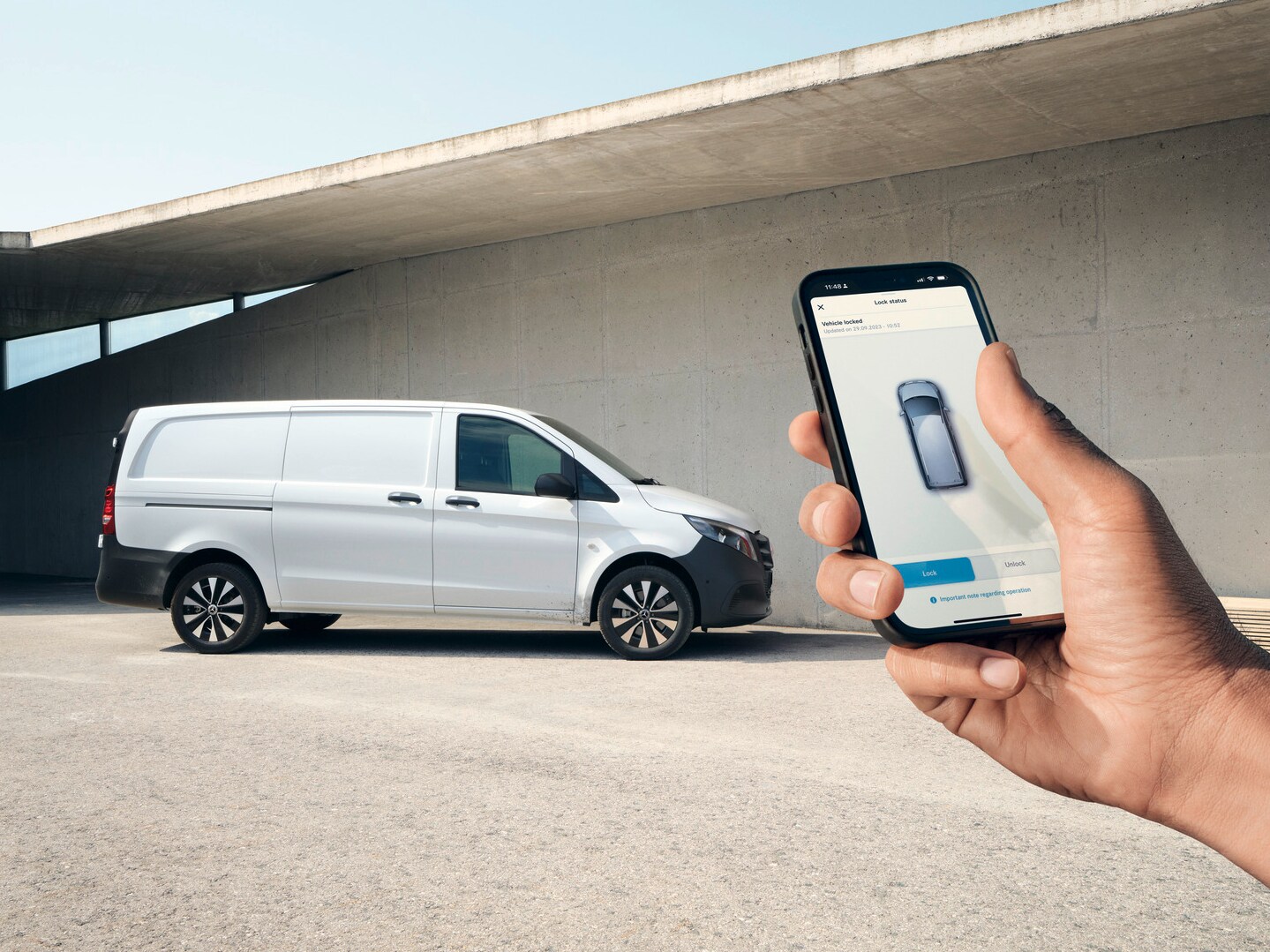 En hand håller upp en smartphone som visar Mercedes me-appen. Vito skåpbil i bakgrunden.