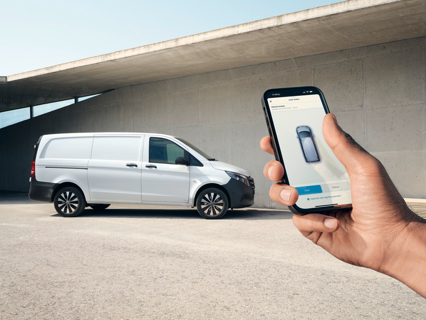 En hand håller upp en smartphone som visar Mercedes me-appen. Vito skåpbil i bakgrunden.