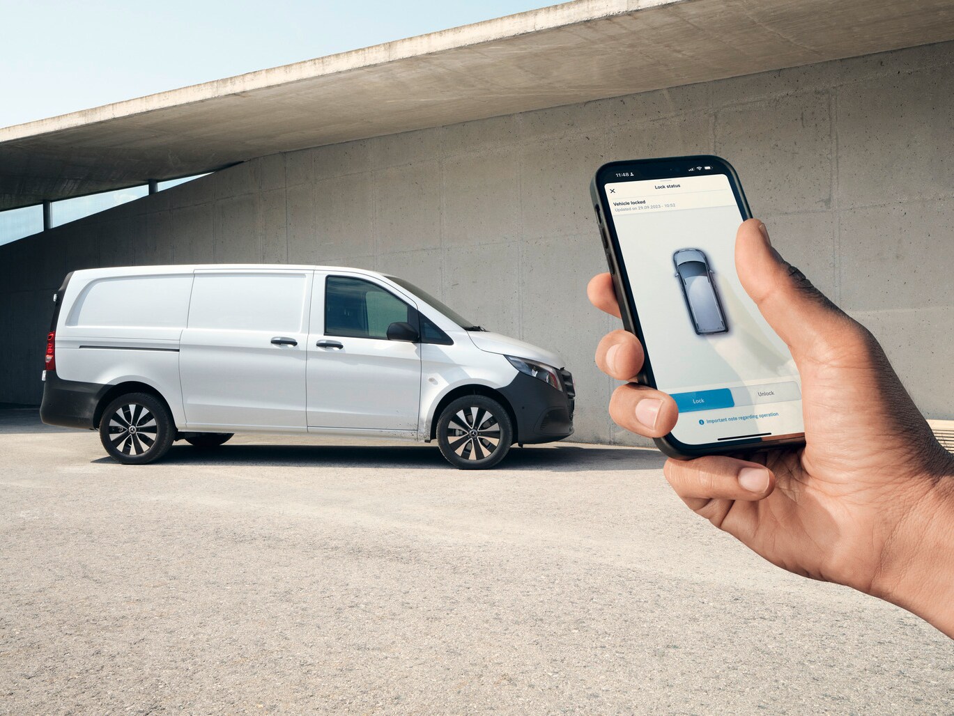 En hand håller upp en smartphone som visar Mercedes me-appen. Vito skåpbil i bakgrunden.