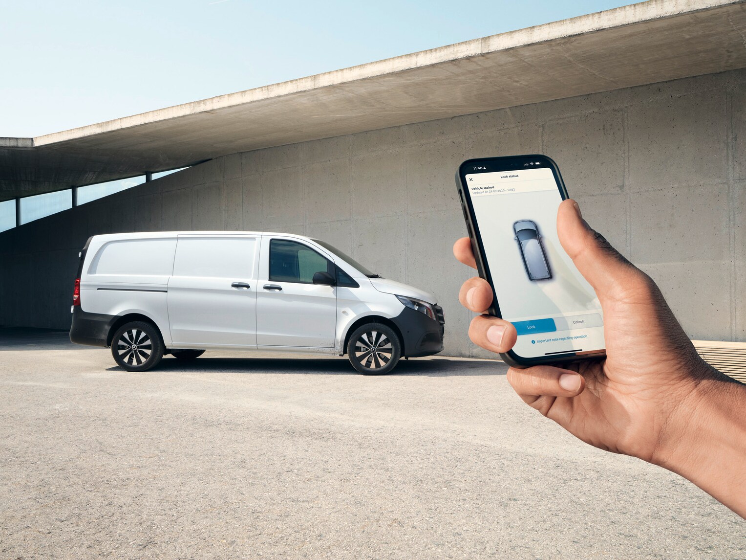 En hand håller upp en smartphone som visar Mercedes me-appen. Vito skåpbil i bakgrunden.