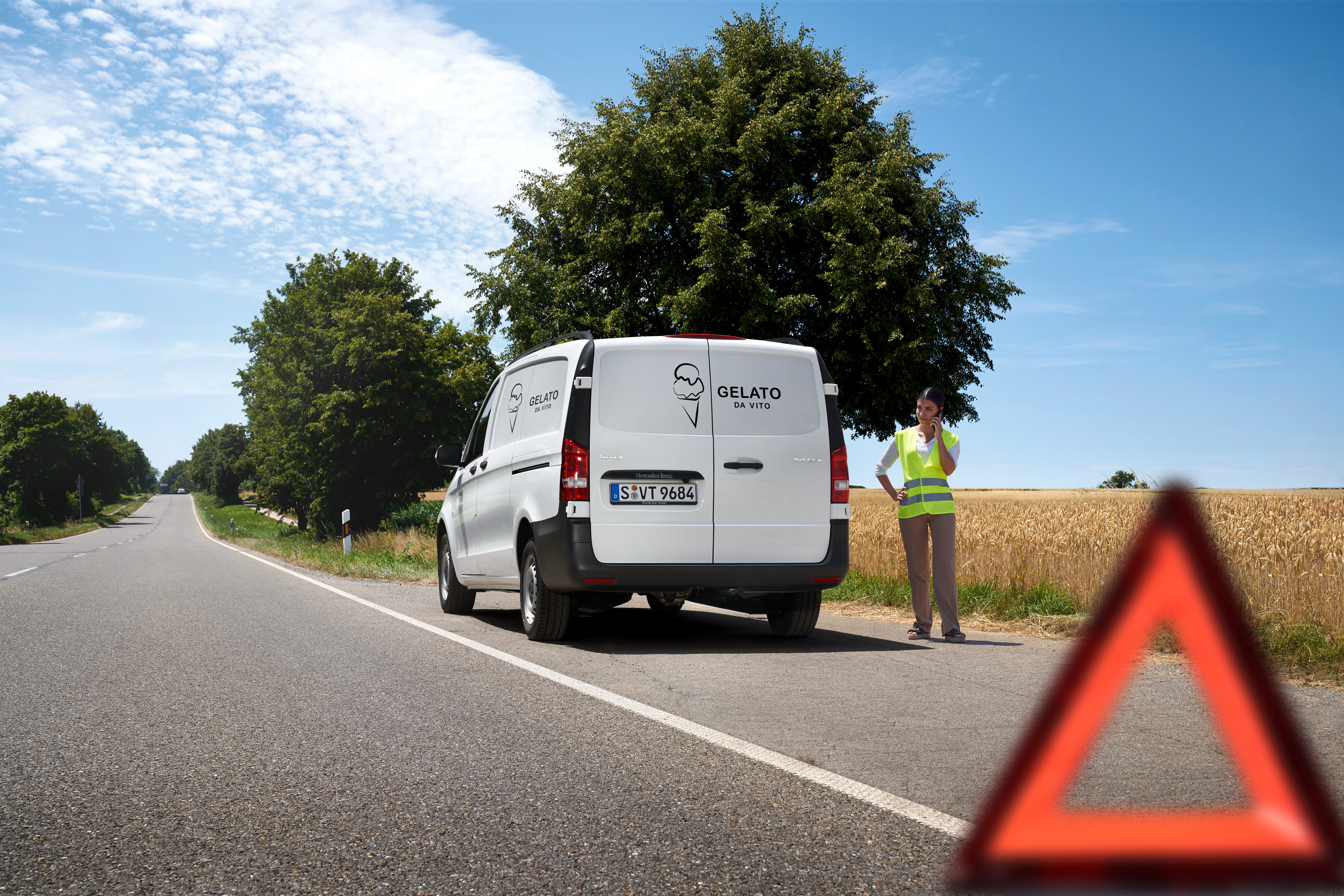 Mercedes-Benz | Vans Care | Service24h A woman calls the Mercedes-Benz service 24h hotline, a Mercedes-Benz Sprinter is stationary by the side of country road.