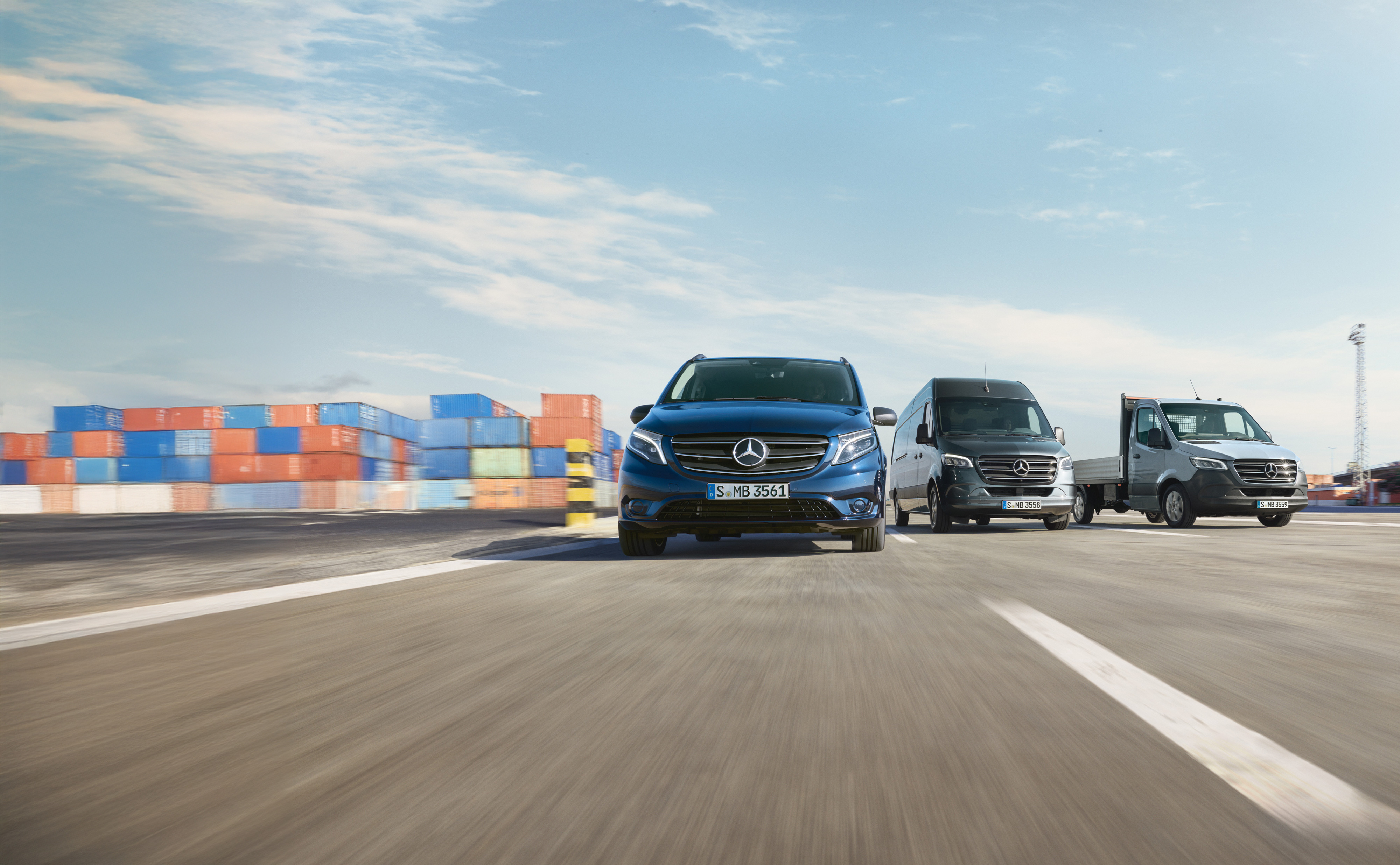 Mercedes-Benz | Vans Care | Service24h Ett antal Mercedes-Benz transportbilar parkerade sida vid sida på en väg intill en lastkaj.