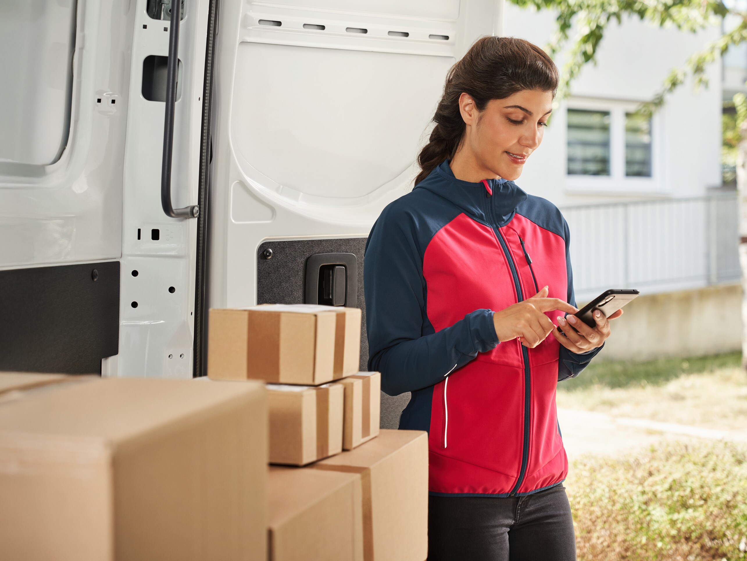 Leveransbud som använder en smartphone framför en budbil med paket.