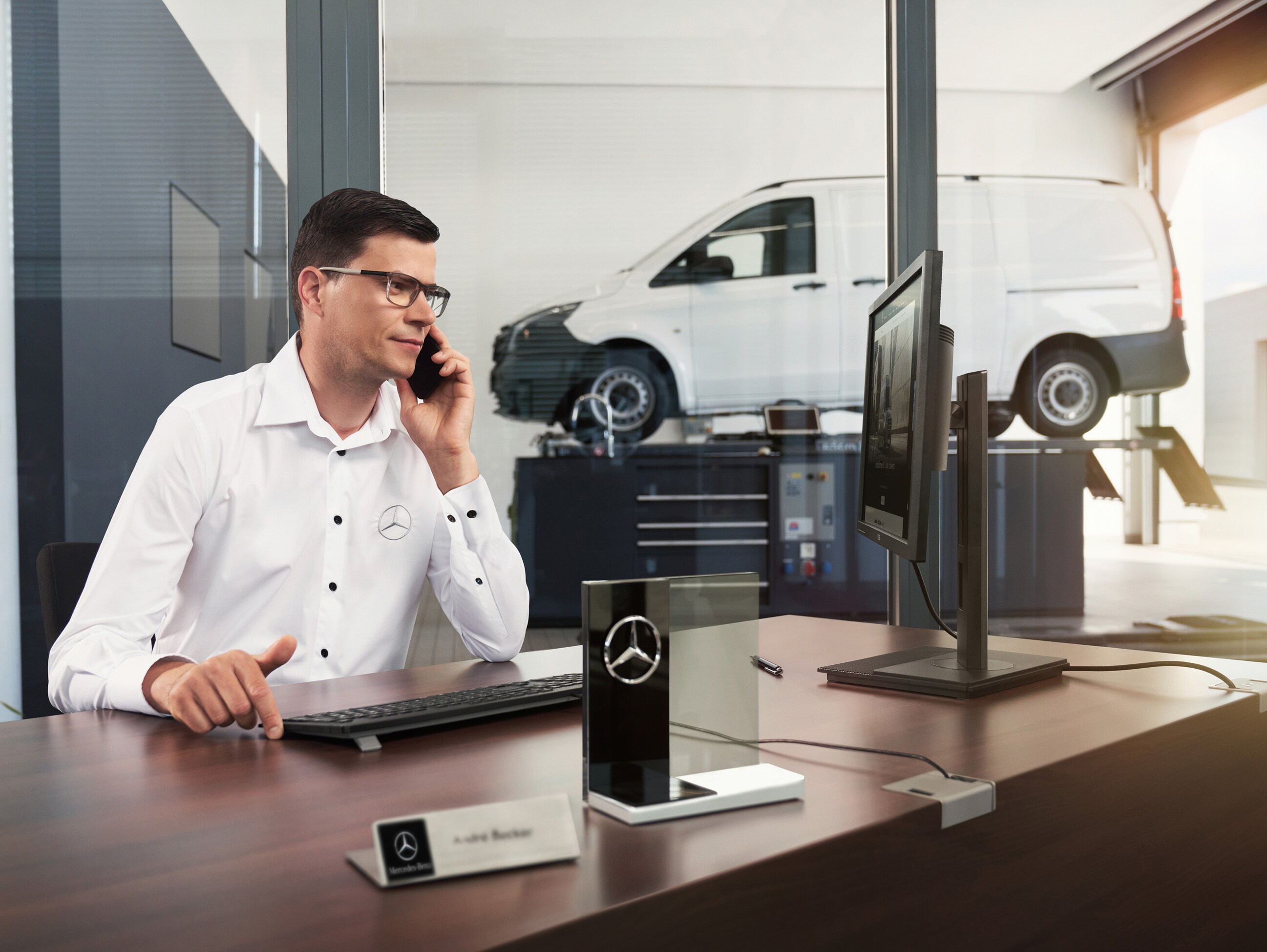 En anställd på Mercedes-Benz pratar i telefon vid ett skrivbord.