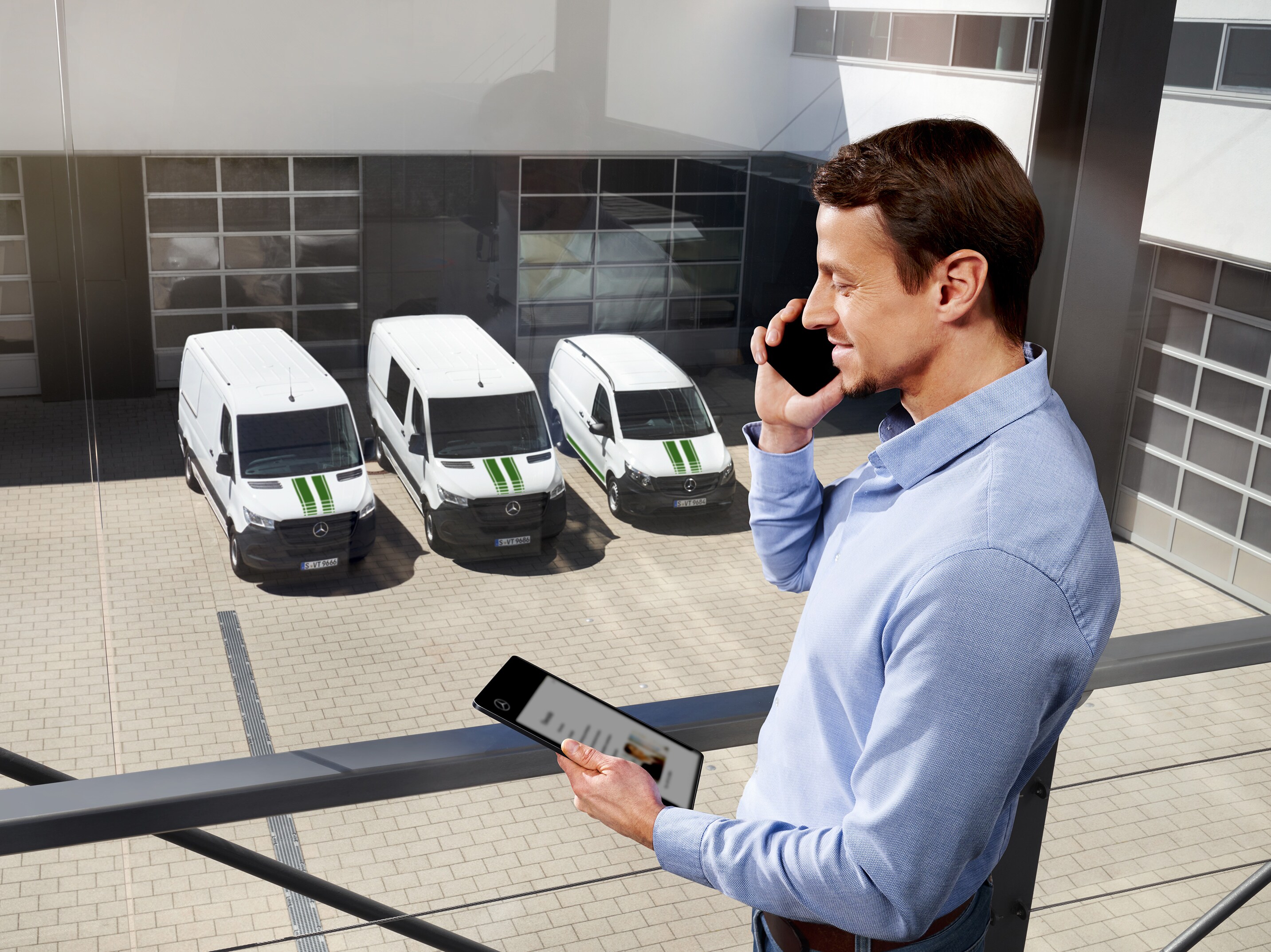Man pratar i mobiltelefon framför en grupp vita Mercedes-Benz transportbilar.