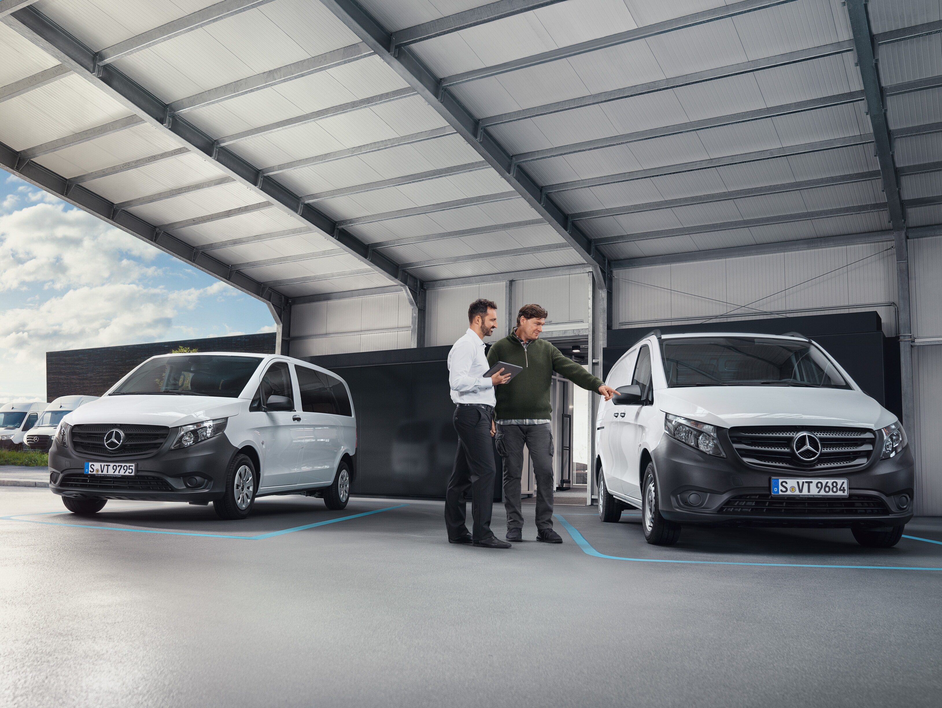 Två personer pratar i ett arbetsrum framför två Mercedes-Benz-transportbilar.