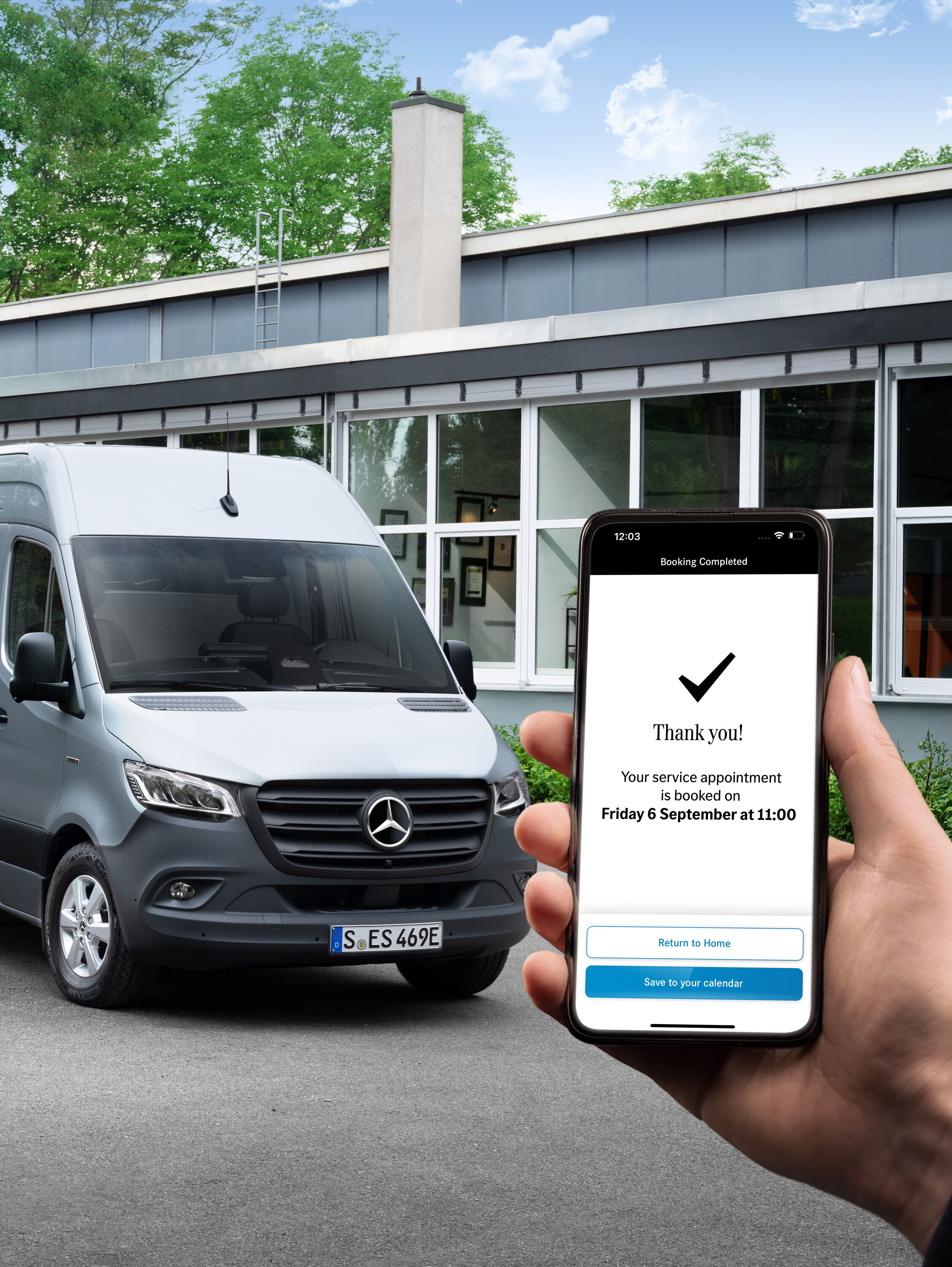 En grå transportbil av märket Mercedes-Benz Sprinter framför ett kontor med en person som håller i en smartphone i förgrunden.