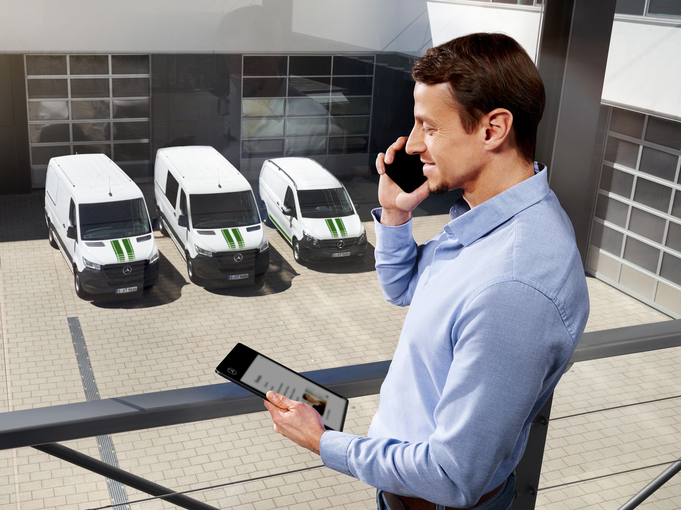 Man pratar i telefon med surfplatta framför tre Mercedes-Benz transportbilar.